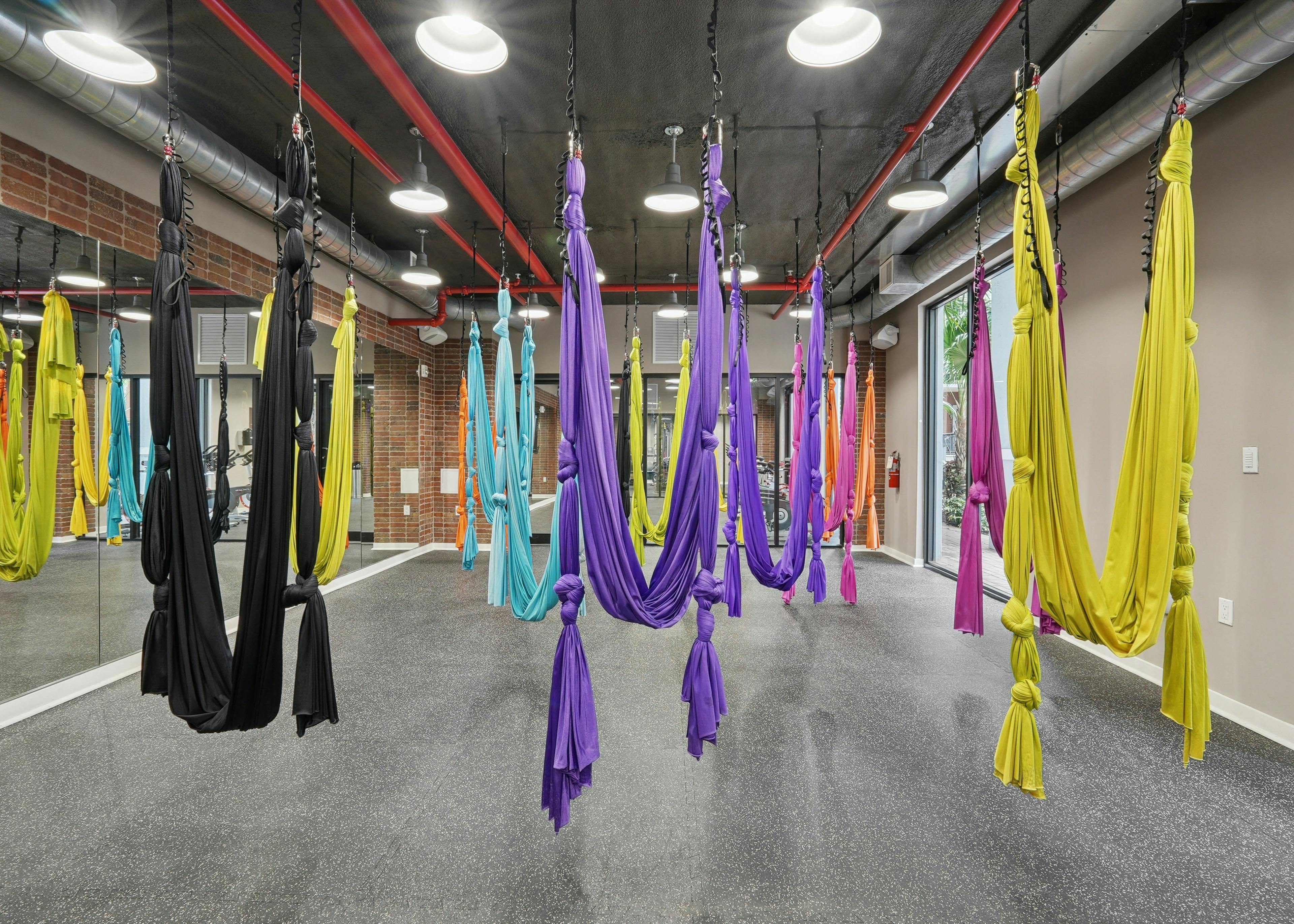 Interior view of an aerial yoga studio with hardwood flooring and floor to ceiling mirrors and a natural brick wall
