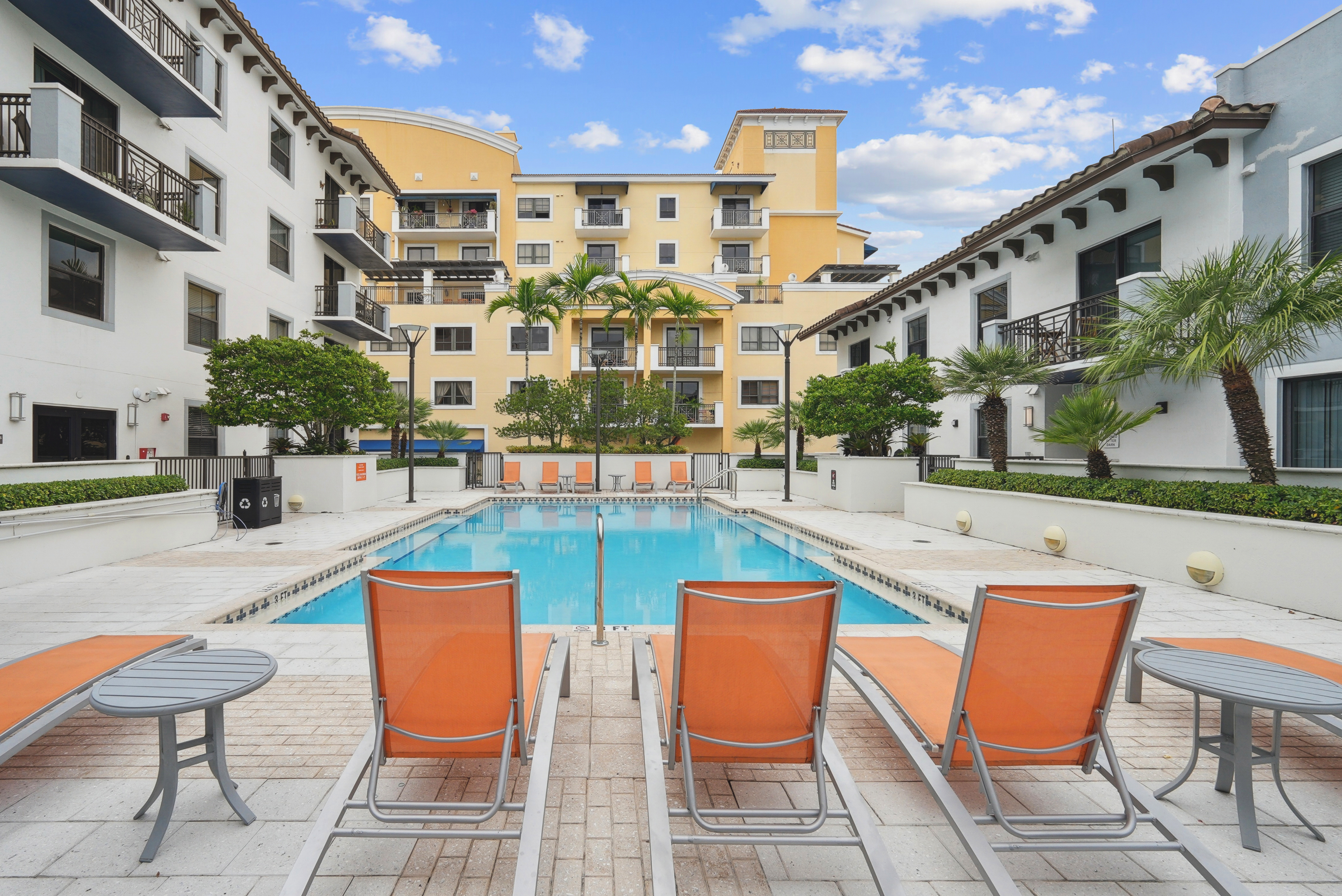 Exterior view of a swimming pool at AMLI Dadeland apartments with orange lounge chairs and lush green plants surrounding