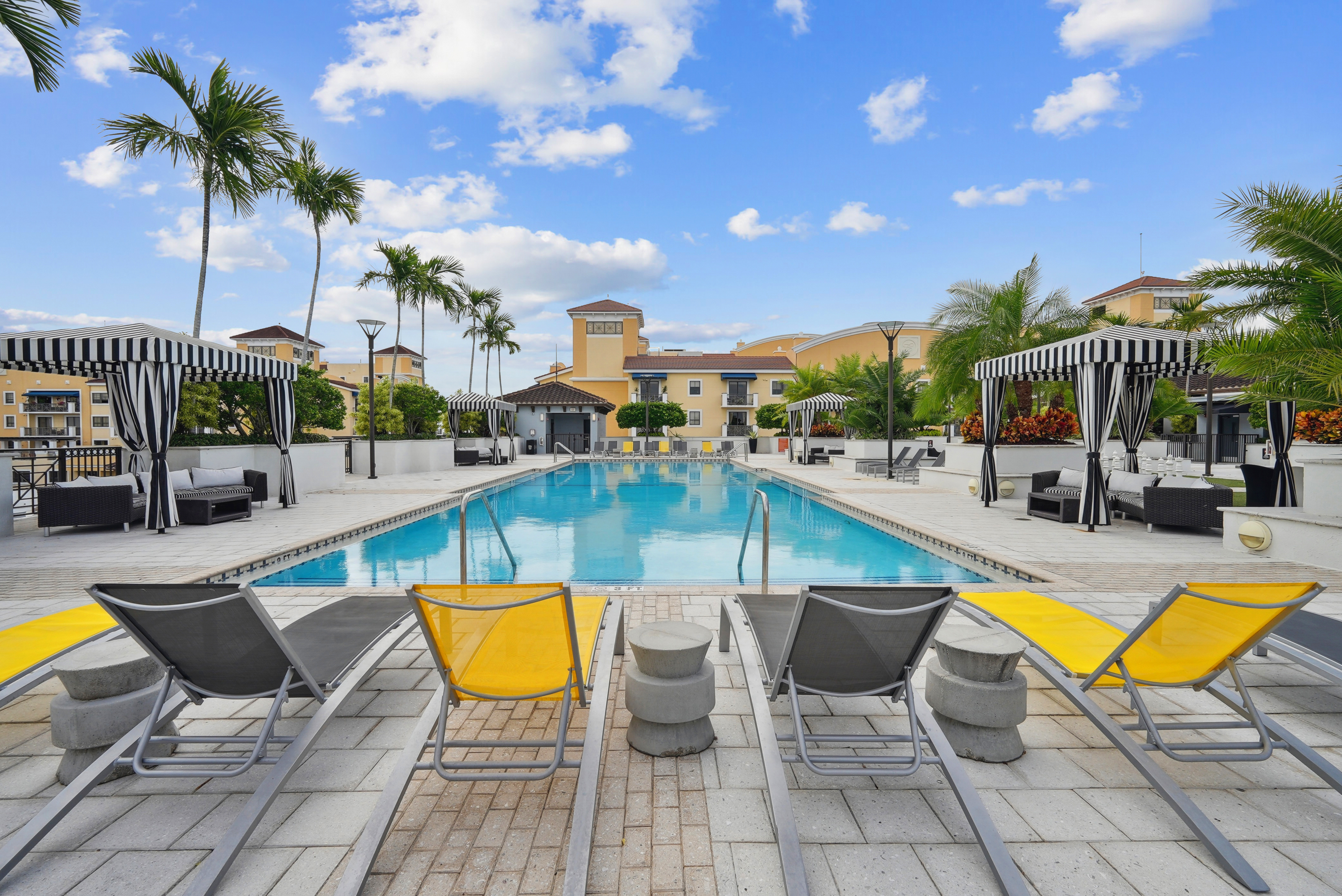 Swimming pool area at AMLI Dadeland apartments with yellow and grey lounge chairs and black and white striped cabanas