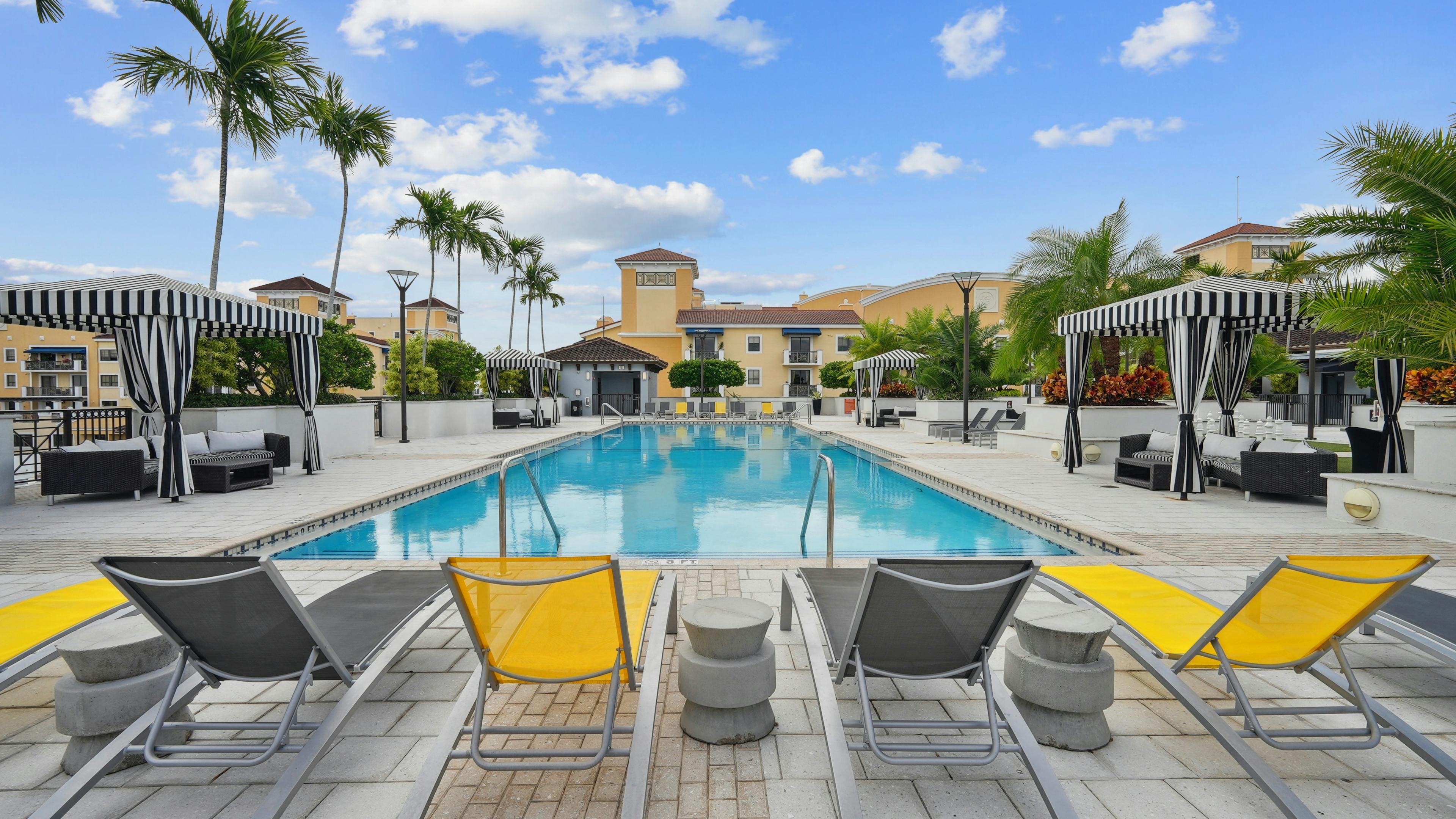 Swimming pool area at AMLI Dadeland apartments with yellow and grey lounge chairs and black and white striped cabanas