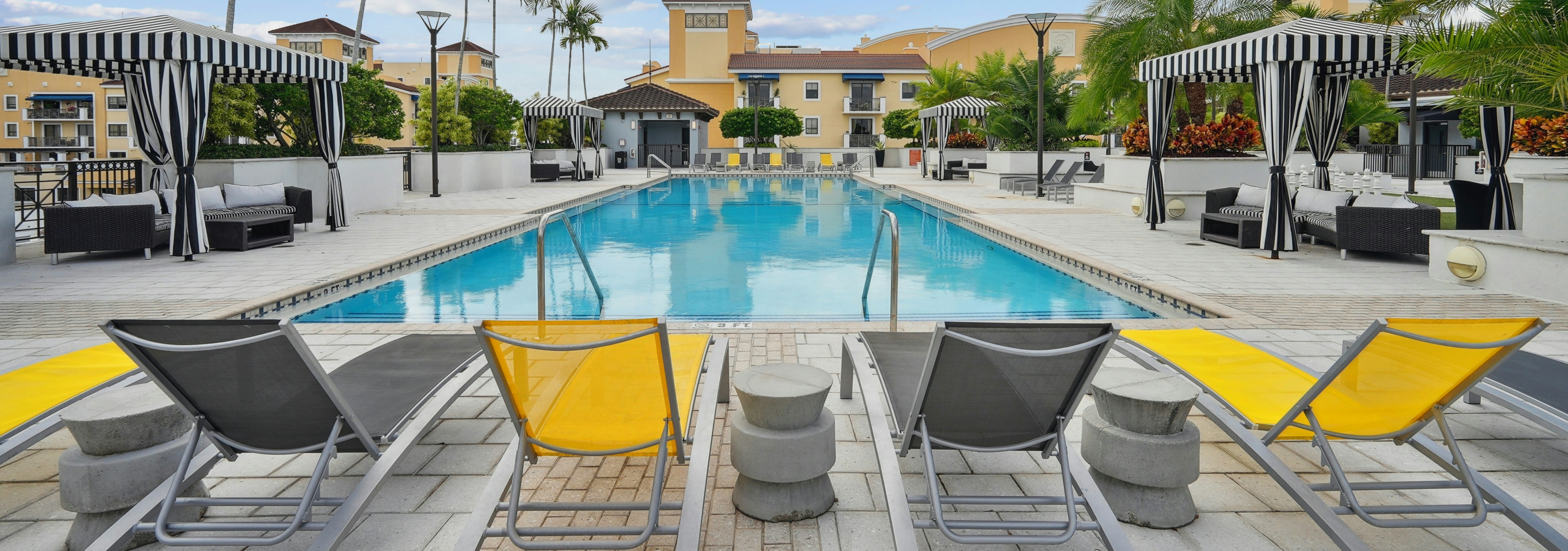 Swimming pool area at AMLI Dadeland apartments with yellow and grey lounge chairs and black and white striped cabanas