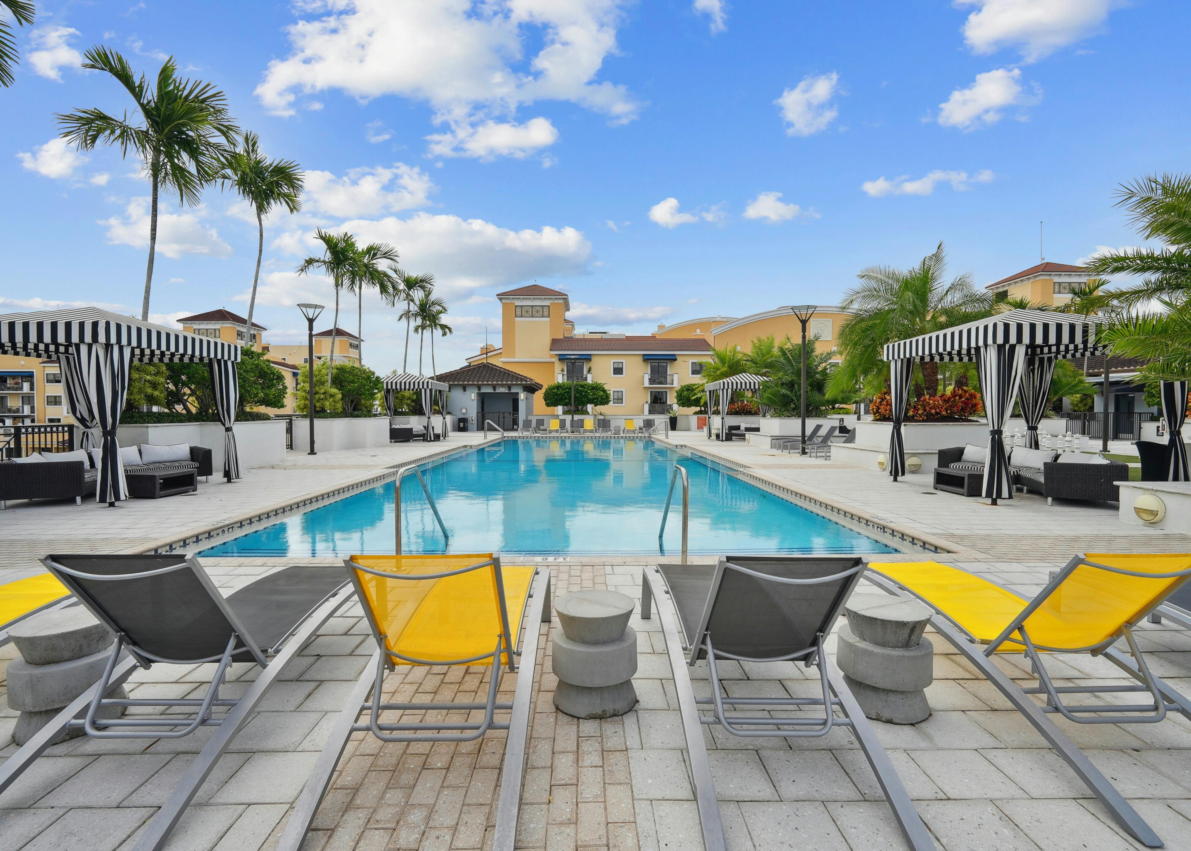 Swimming pool area at AMLI Dadeland apartments with yellow and grey lounge chairs and black and white striped cabanas
