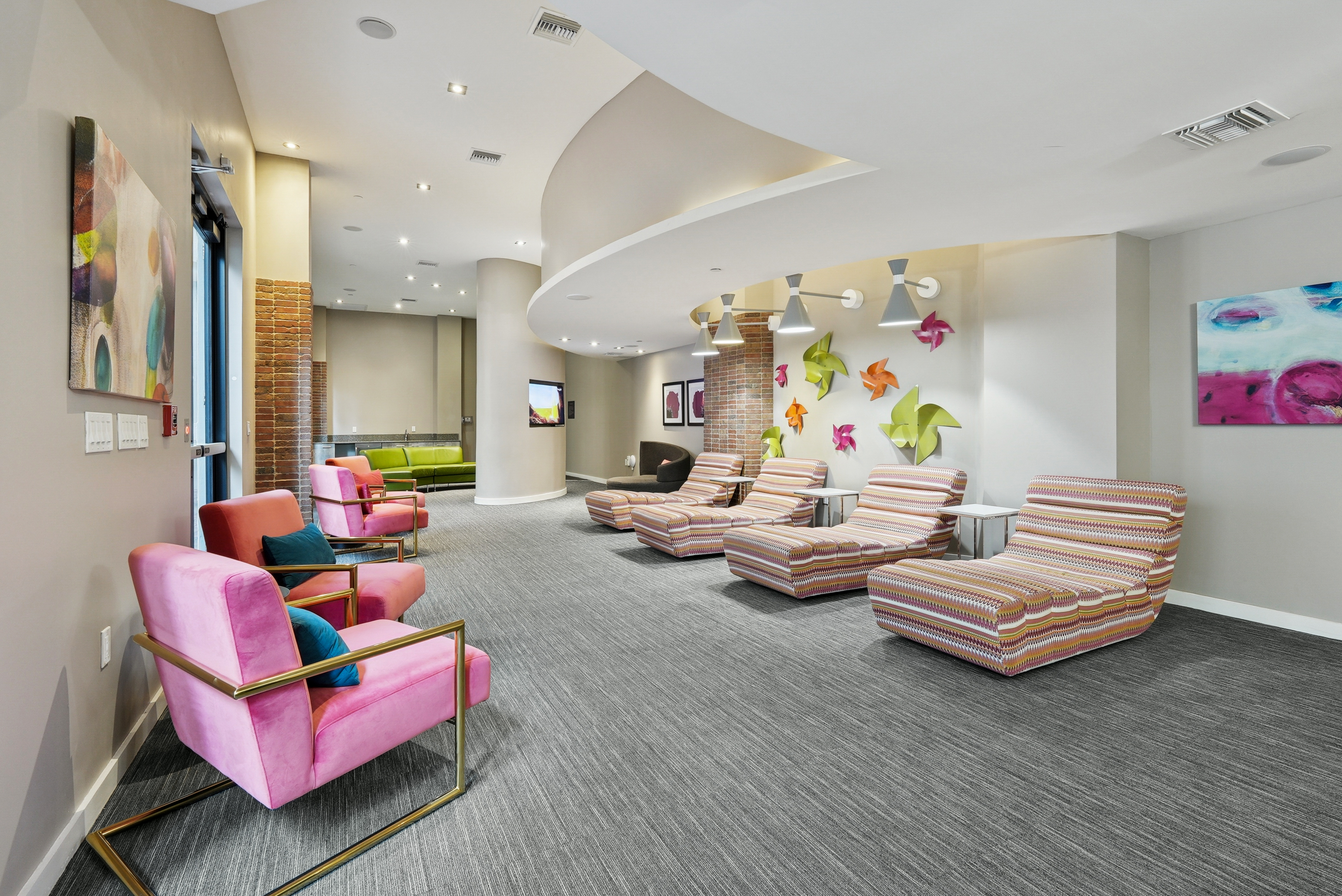 AMLI Dadeland apartments resident lounge space with colorful plush chairs and grey carpeting and various wall artwork