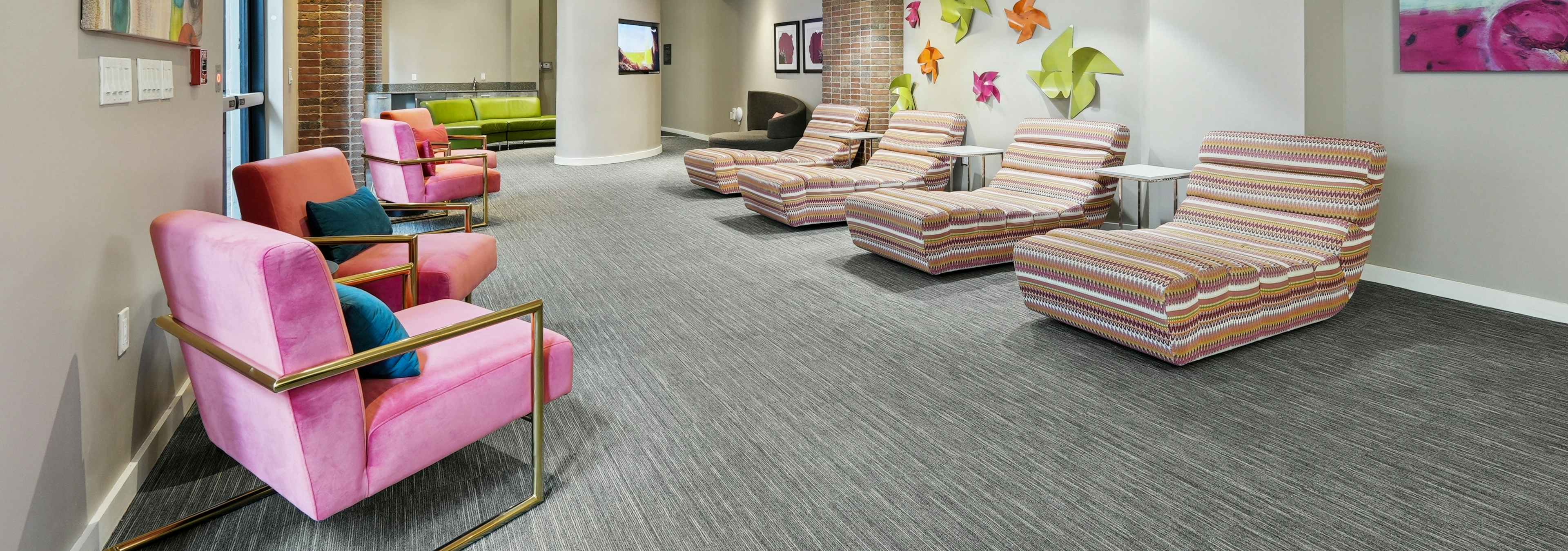 AMLI Dadeland apartments resident lounge space with colorful plush chairs and grey carpeting and various wall artwork
