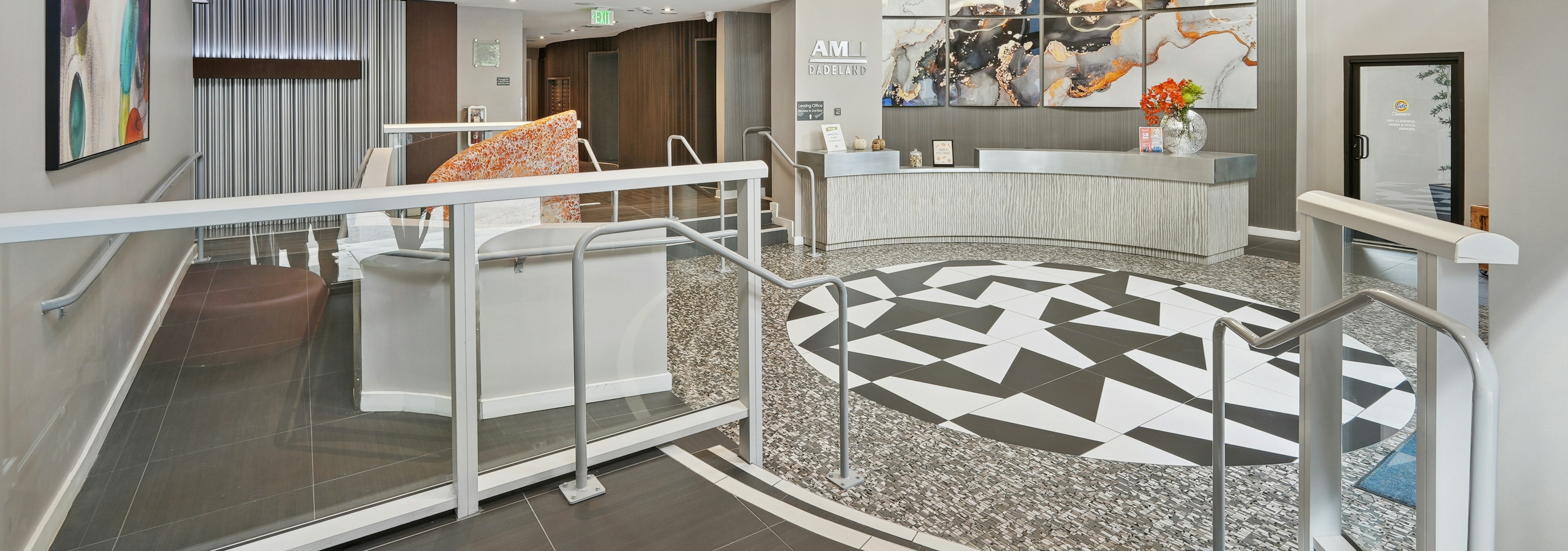 Interior view of the leasing office at AMLI Dadeland apartments with a curved front desk with flowers and vibrant wall art