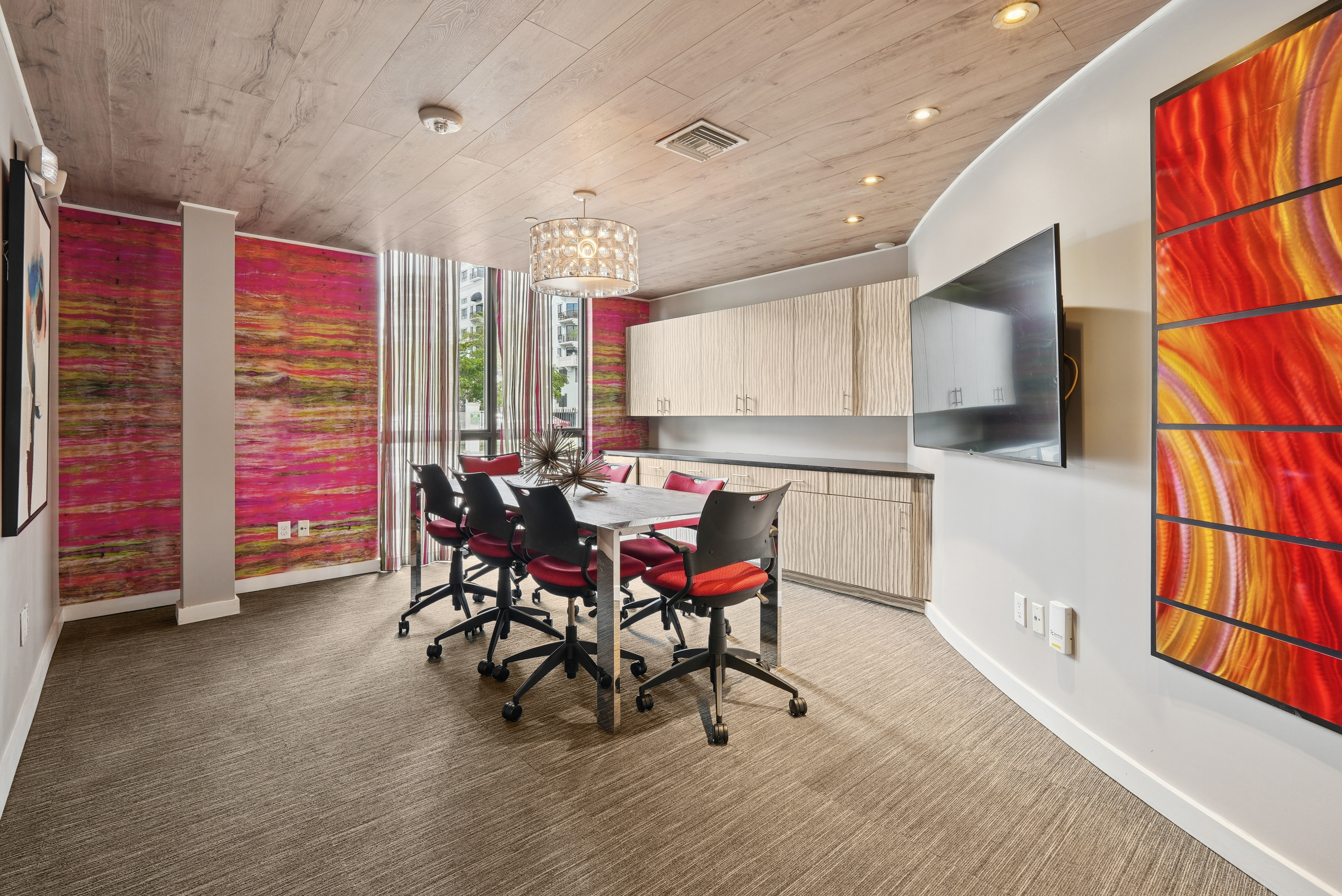 Conference room at AMLI Dadeland apartments with a table and seven chairs and decorative lamp overhead and colorful wallpaper