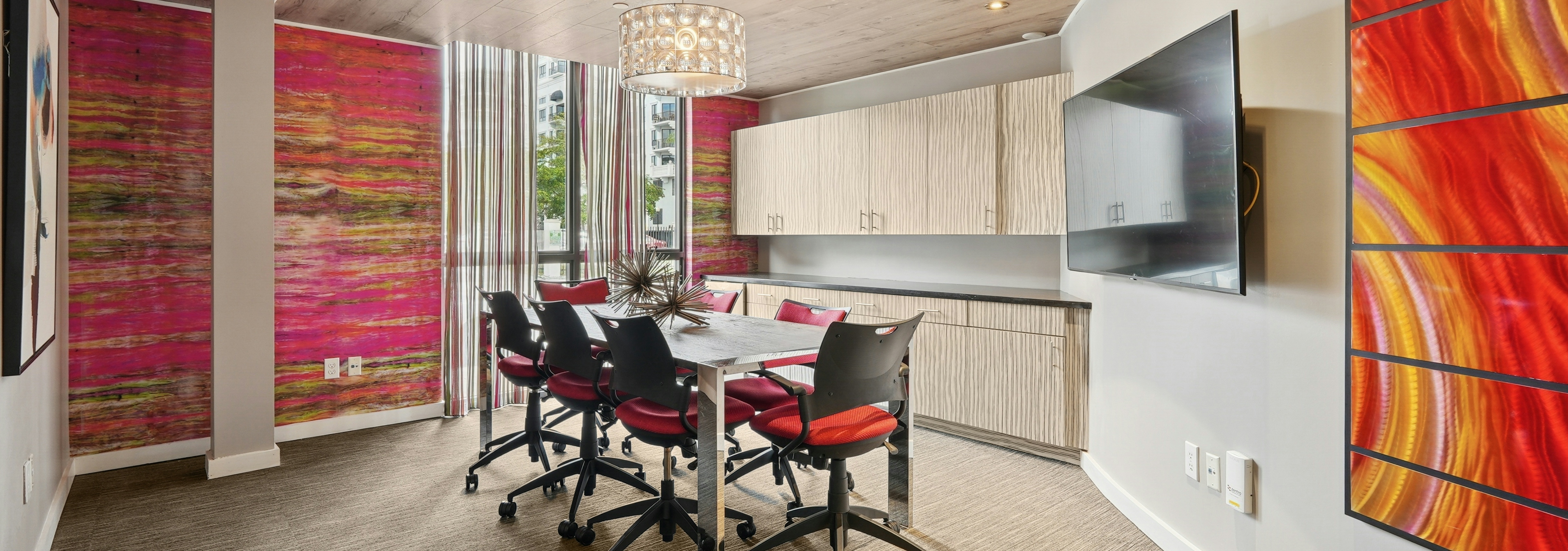 Conference room at AMLI Dadeland apartments with a table and seven chairs and decorative lamp overhead and colorful wallpaper