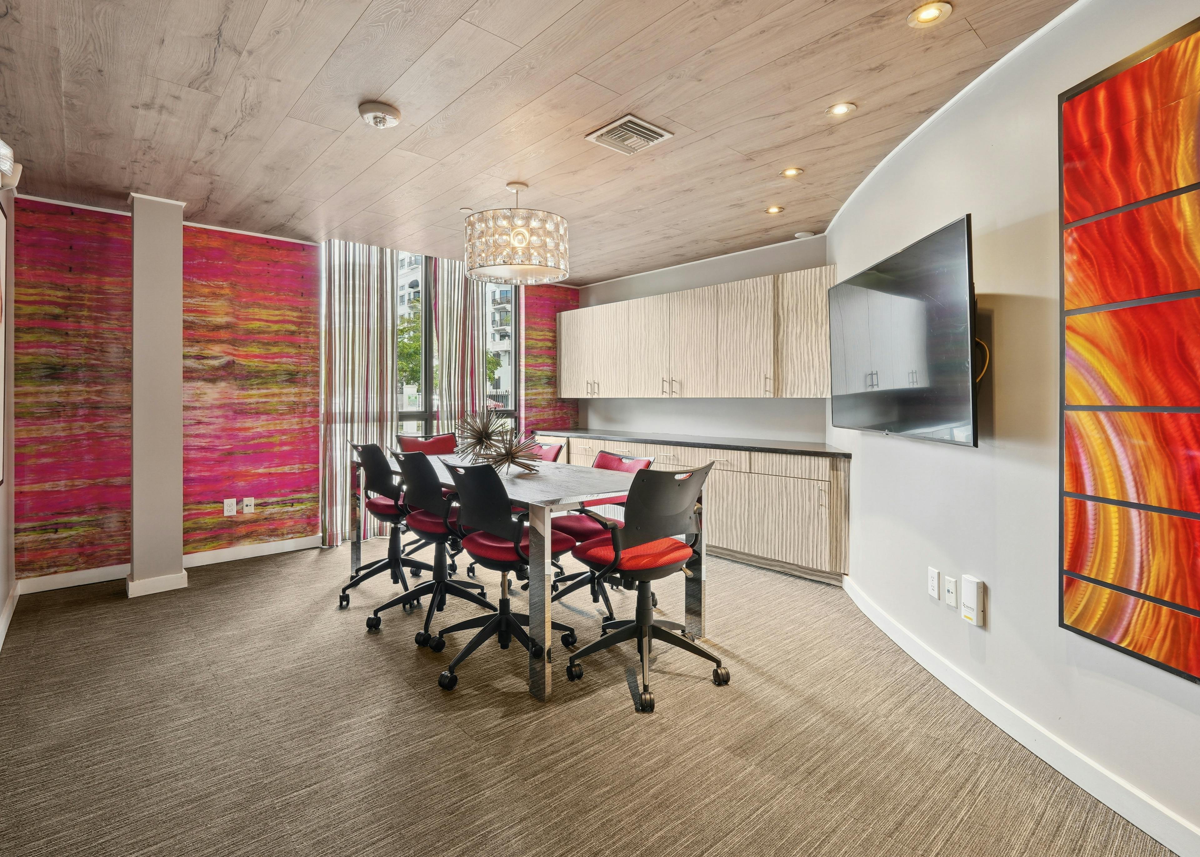 Conference room at AMLI Dadeland apartments with a table and seven chairs and decorative lamp overhead and colorful wallpaper