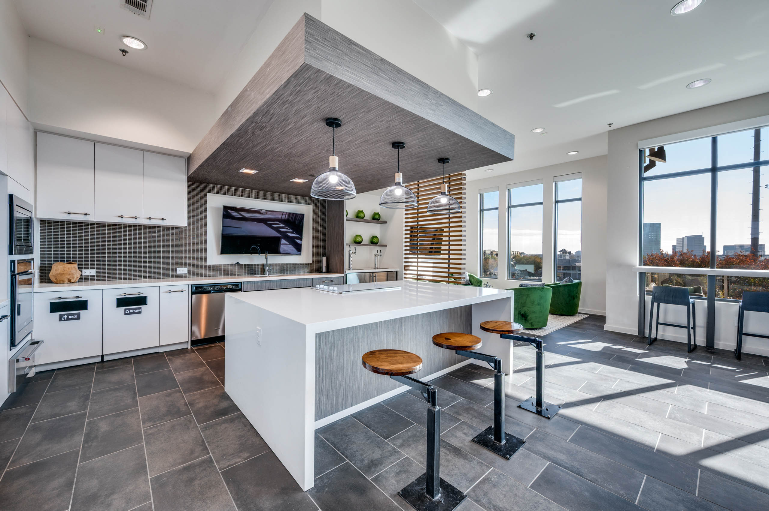 Interior view of AMLI Frisco Crossing apartment sky lounge kitchen with island, pendant lights, bolted barstools, and stainless appliances.