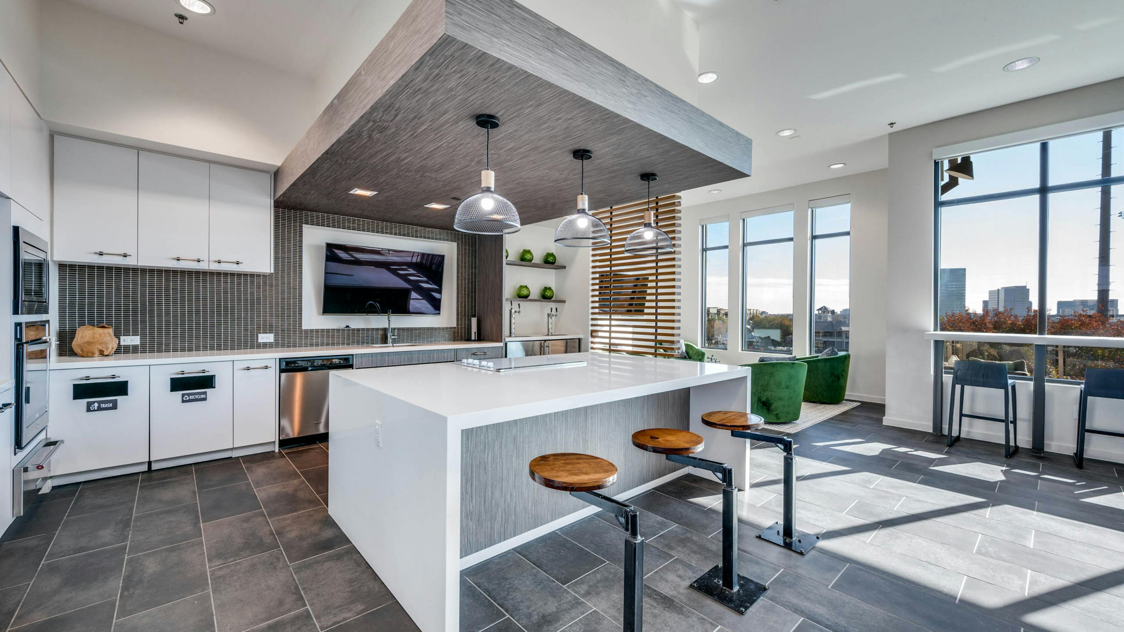 Interior view of AMLI Frisco Crossing apartment sky lounge kitchen with island, pendant lights, bolted barstools, and stainless appliances.