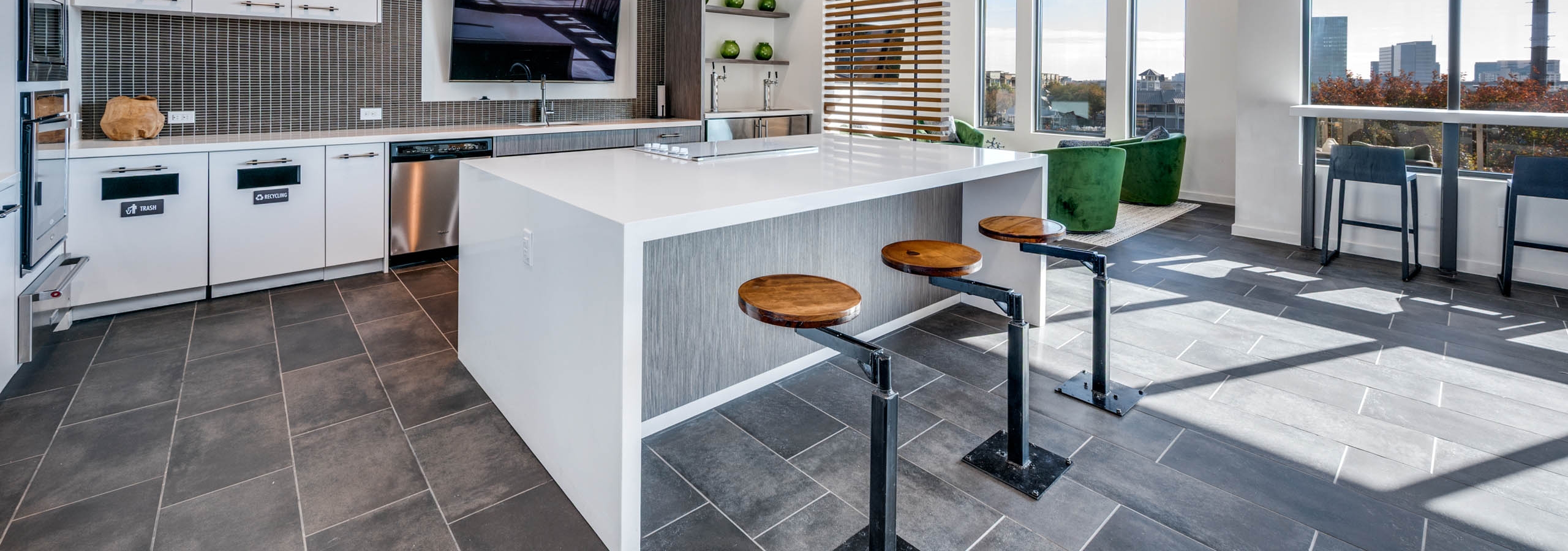 Interior view of AMLI Frisco Crossing apartment sky lounge kitchen with island, pendant lights, bolted barstools, and stainless appliances.