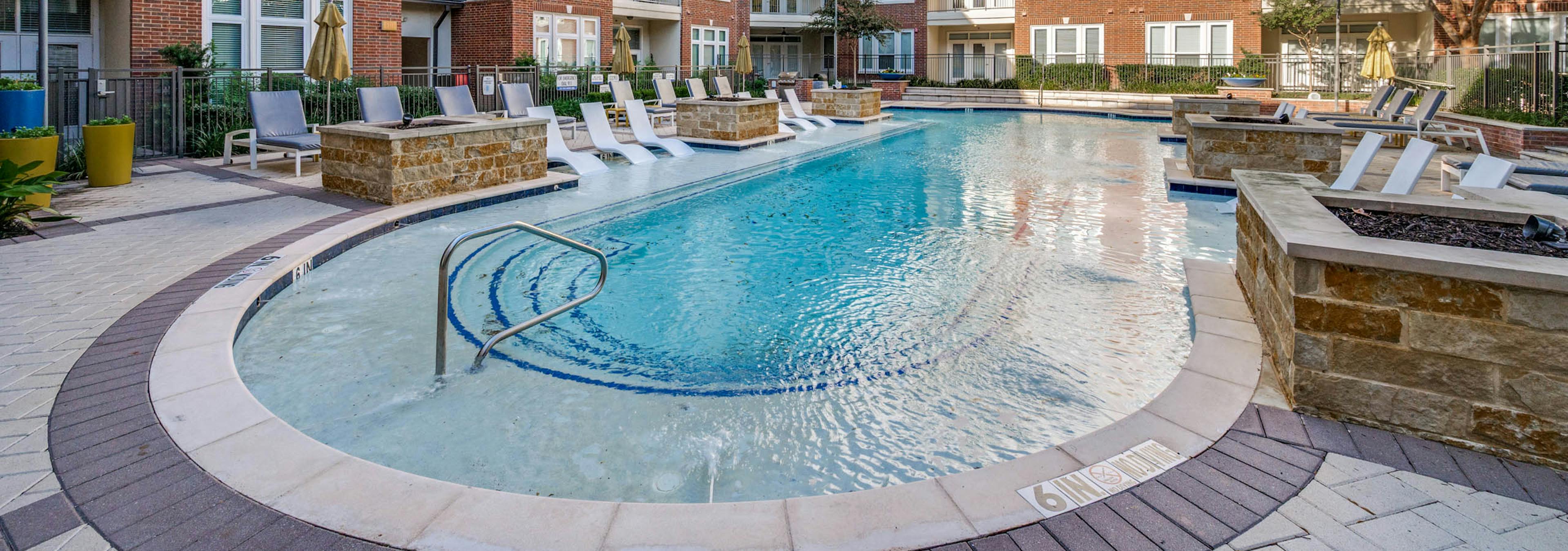 AMLI Frisco Crossing apartment daytime pool view with tanning ledge, lounge seating, and surrounding red brick buildings and trees.