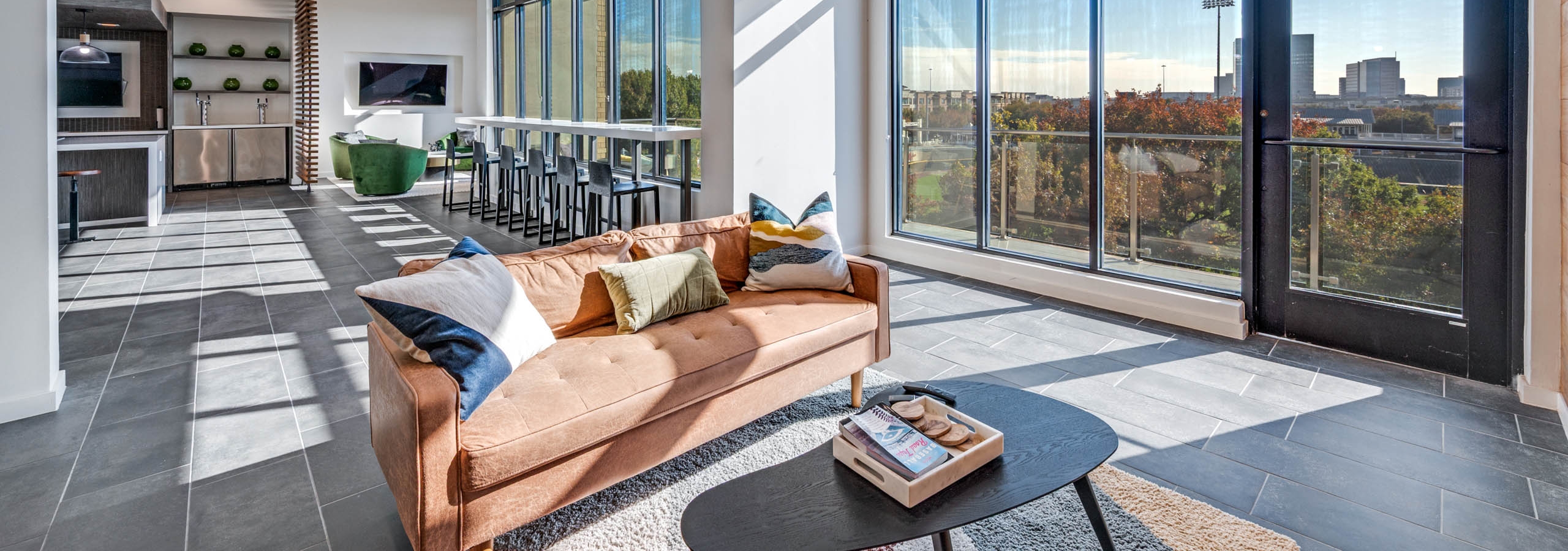 Spacious lounge area with large windows, bar seating, plush tan sofa over a decorative rug at AMLI Frisco Crossing apartment sky lounge.