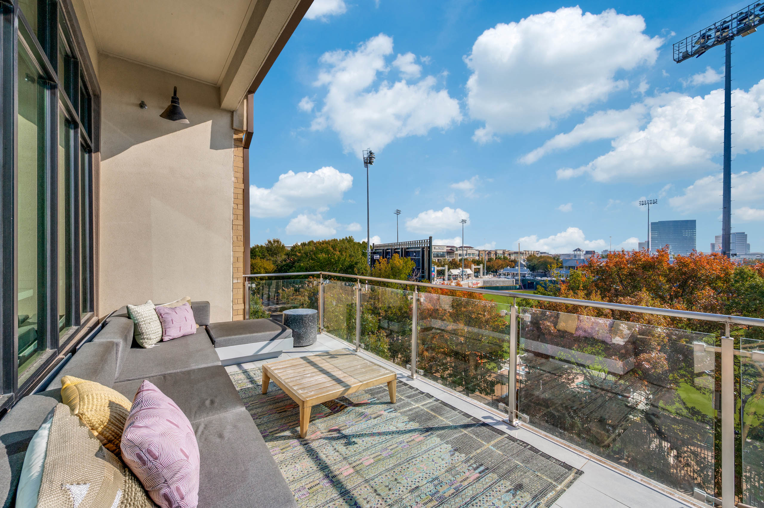 Balcony lounge area with plush sectional sofa, throw pillows, coffee table, and stadium views at AMLI Frisco Crossing apartments.