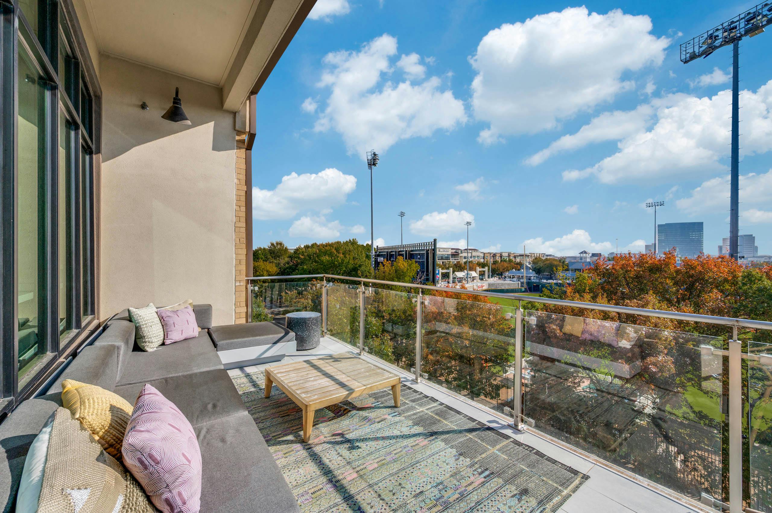 Balcony lounge area with plush sectional sofa, throw pillows, coffee table, and stadium views at AMLI Frisco Crossing apartments.