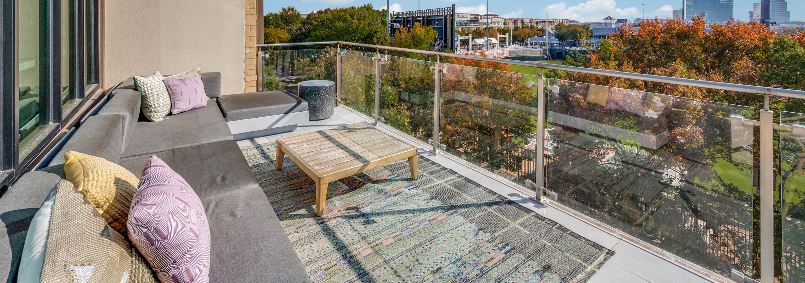 Balcony lounge area with plush sectional sofa, throw pillows, coffee table, and stadium views at AMLI Frisco Crossing apartments.