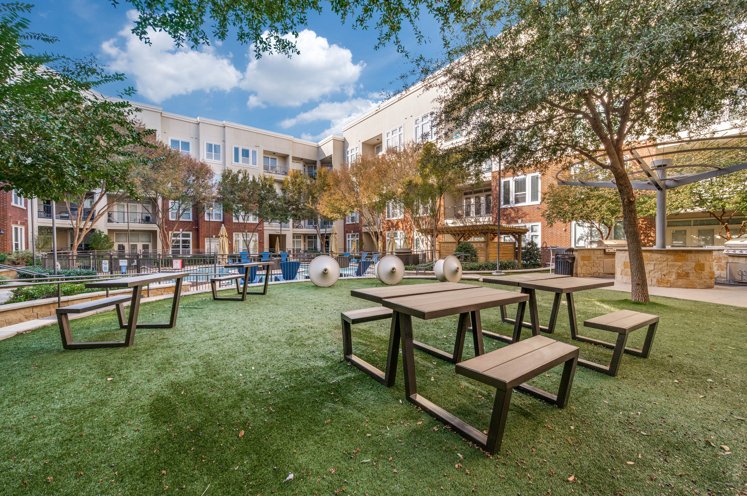 Outdoor courtyard lawn with picnic tables, sculptural seating, and barbecue grills overlooking the pool at AMLI Frisco Crossing apartments