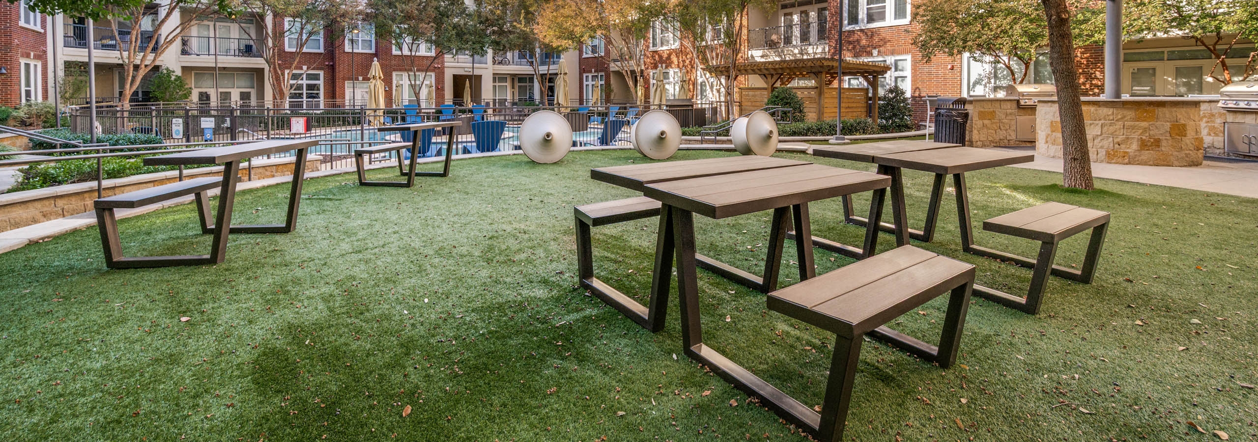 Outdoor courtyard lawn with picnic tables, sculptural seating, and barbecue grills overlooking the pool at AMLI Frisco Crossing apartments