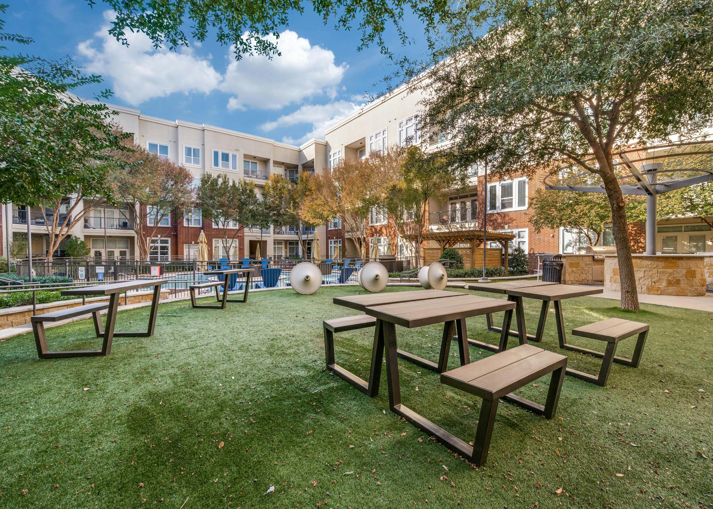 Outdoor courtyard lawn with picnic tables, sculptural seating, and barbecue grills overlooking the pool at AMLI Frisco Crossing apartments