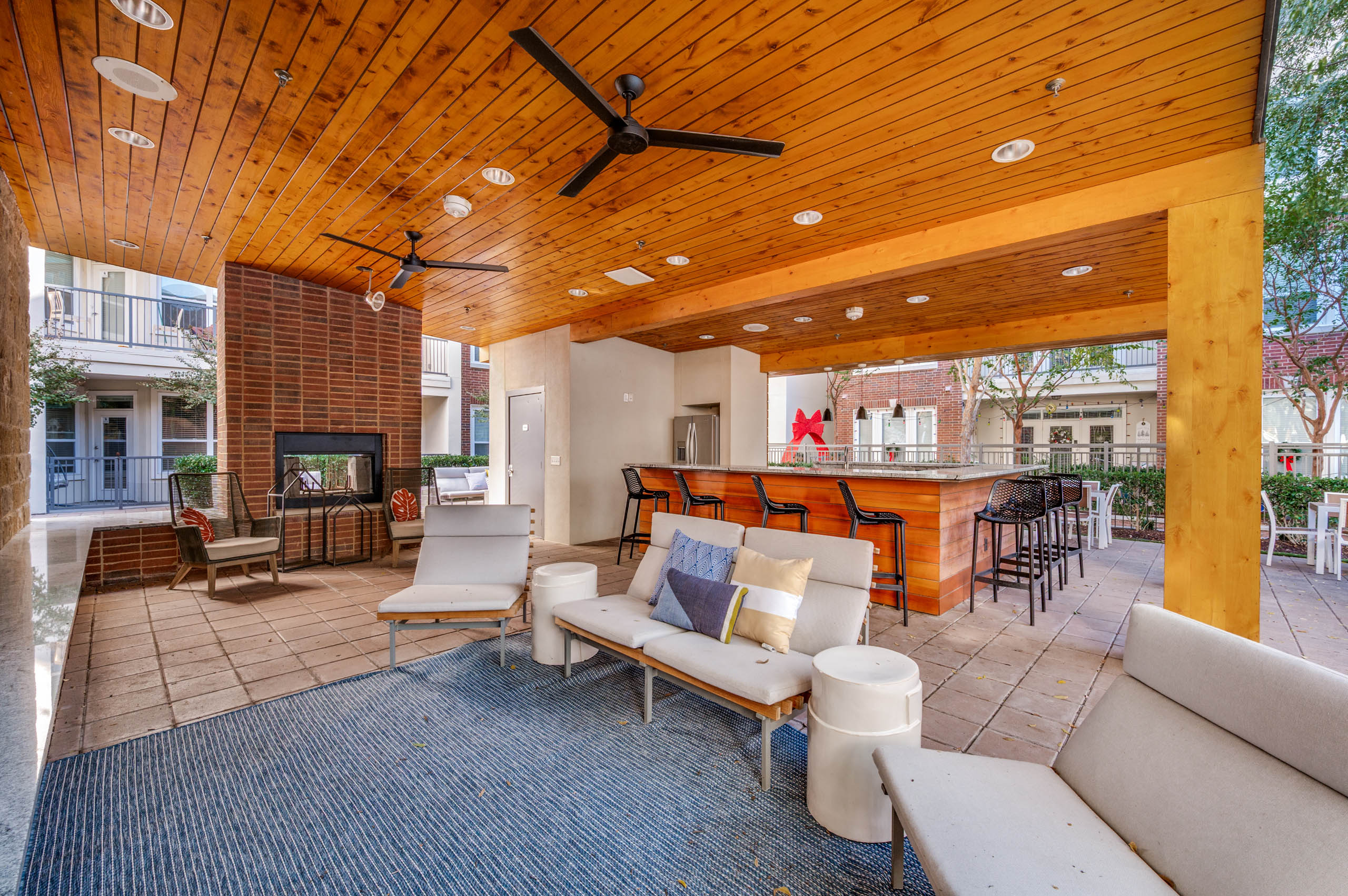 Shaded outdoor lounge area with ceiling fans, cushioned seating, brick fireplace, and bar at AMLI Frisco Crossing apartments