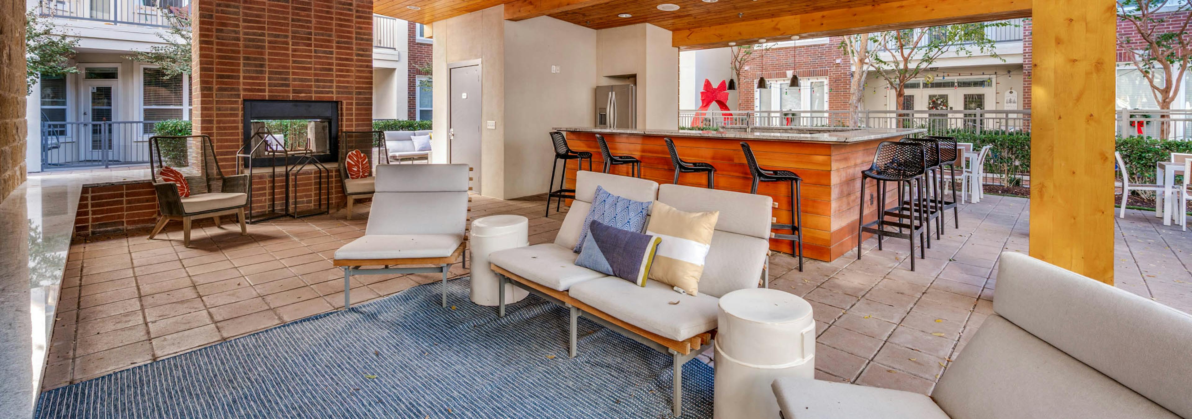 Shaded outdoor lounge area with ceiling fans, cushioned seating, brick fireplace, and bar at AMLI Frisco Crossing apartments