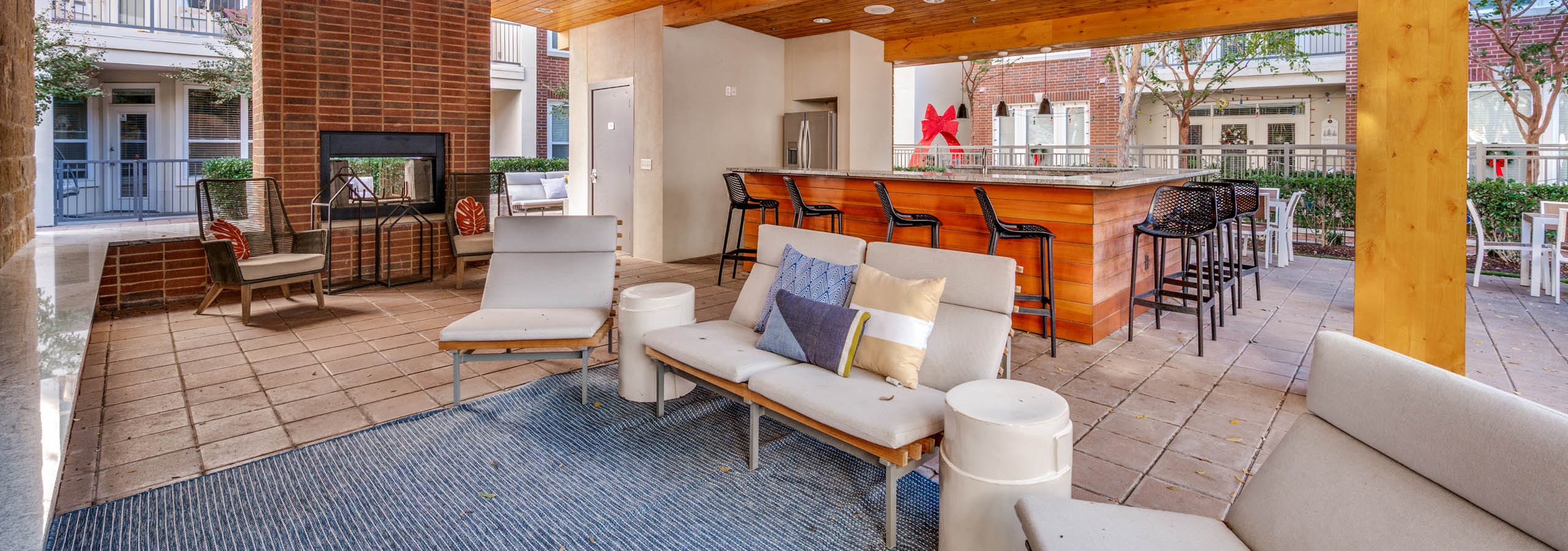 Shaded outdoor lounge area with ceiling fans, cushioned seating, brick fireplace, and bar at AMLI Frisco Crossing apartments