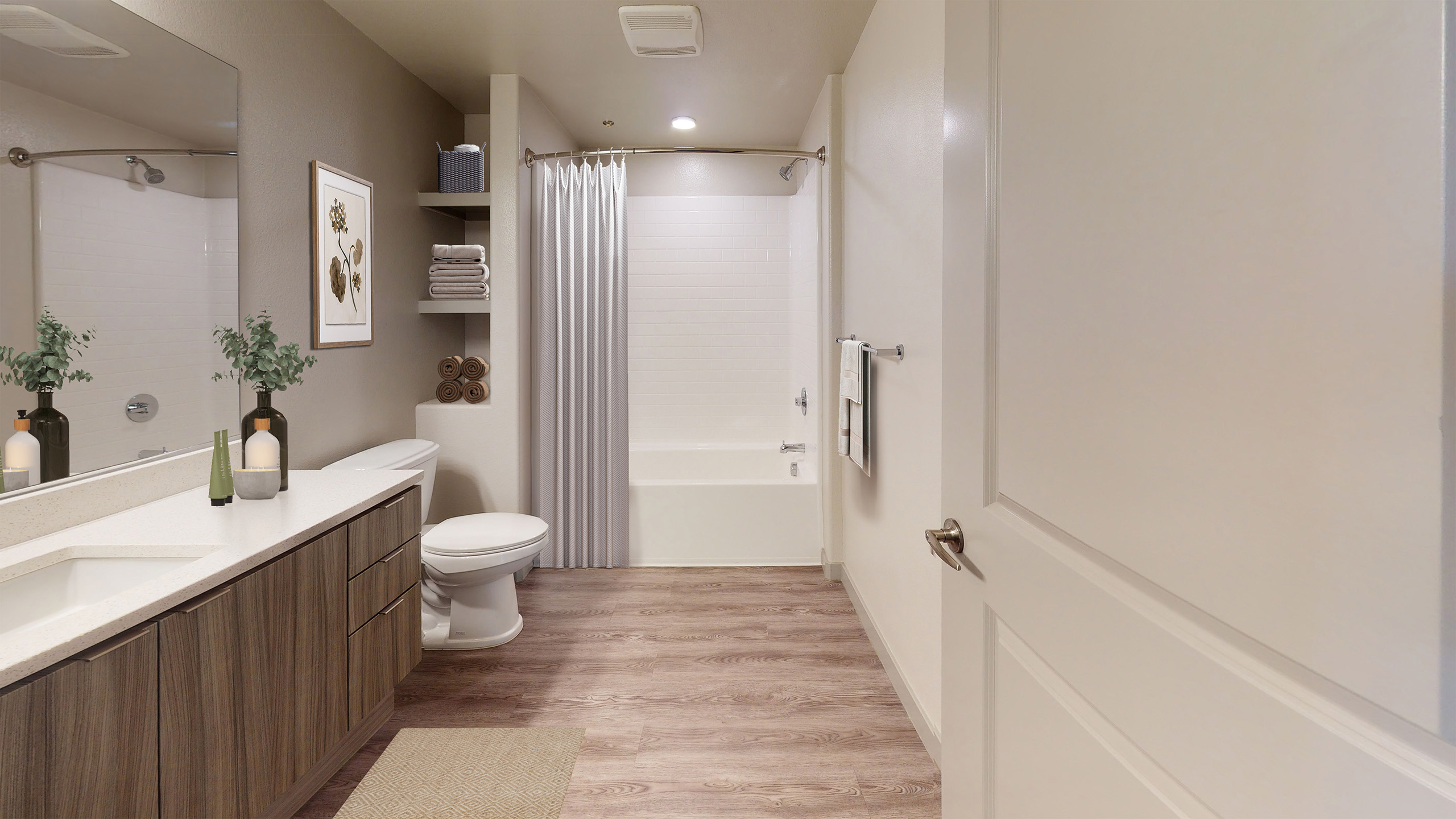 Interior view of AMLI Camarillo apartment bathroom with quartz countertop vanity, wall shelving with towels, and tub with white tile shower.