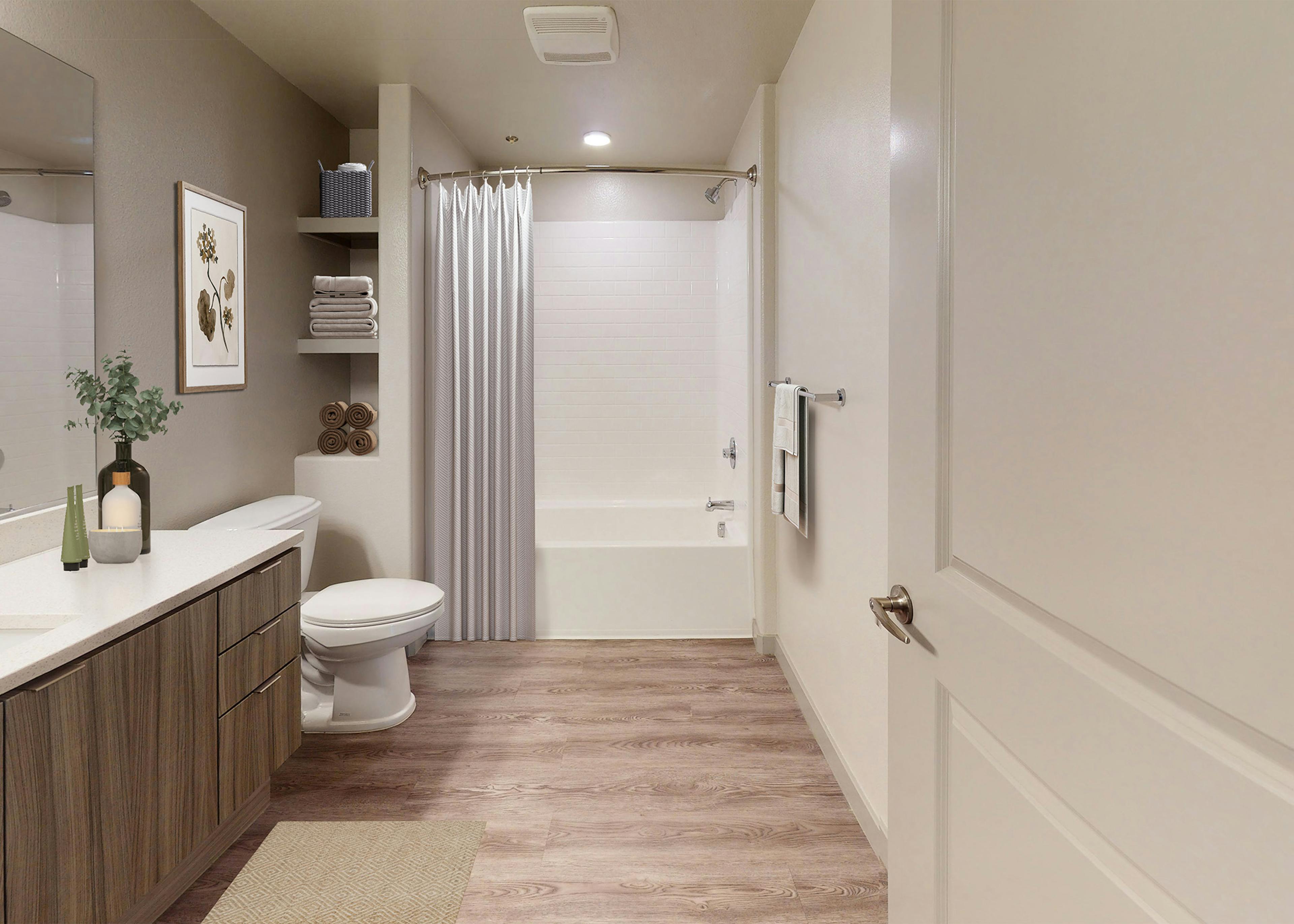 Interior view of AMLI Camarillo apartment bathroom with quartz countertop vanity, wall shelving with towels, and tub with white tile shower.