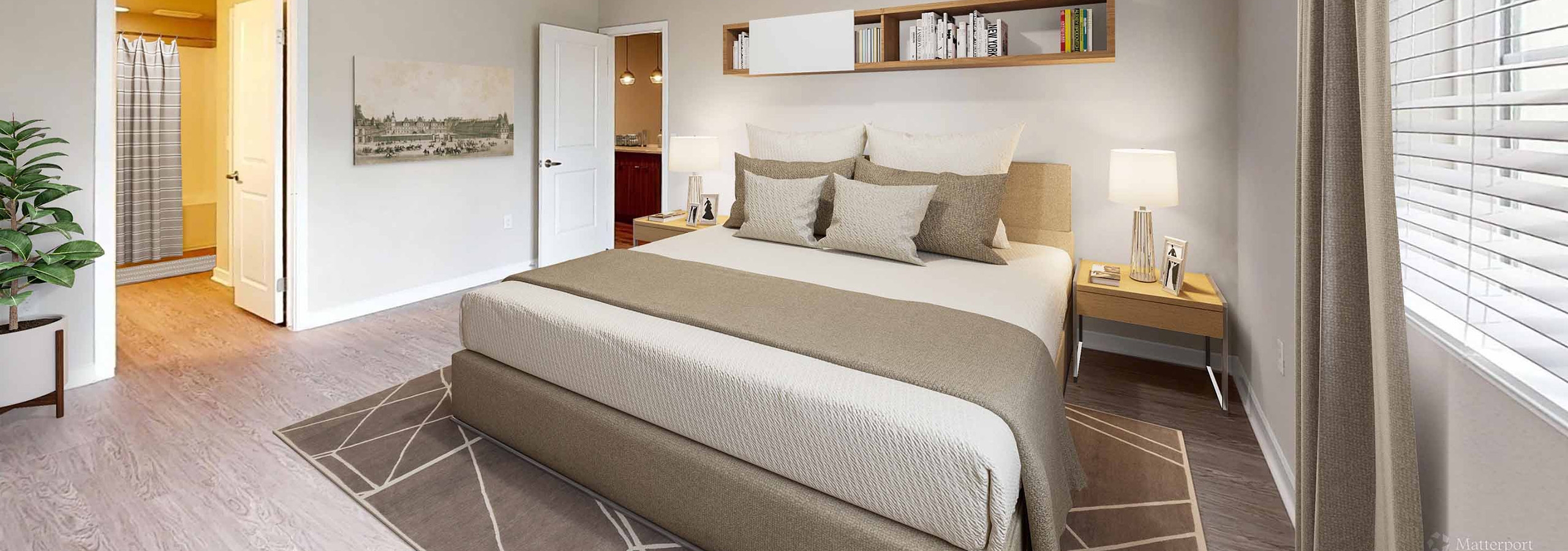 AMLI Camarillo apartment bedroom with king bed, floating bookshelf, two nightstands, potted plant, wall art and glimpse into the bathroom.