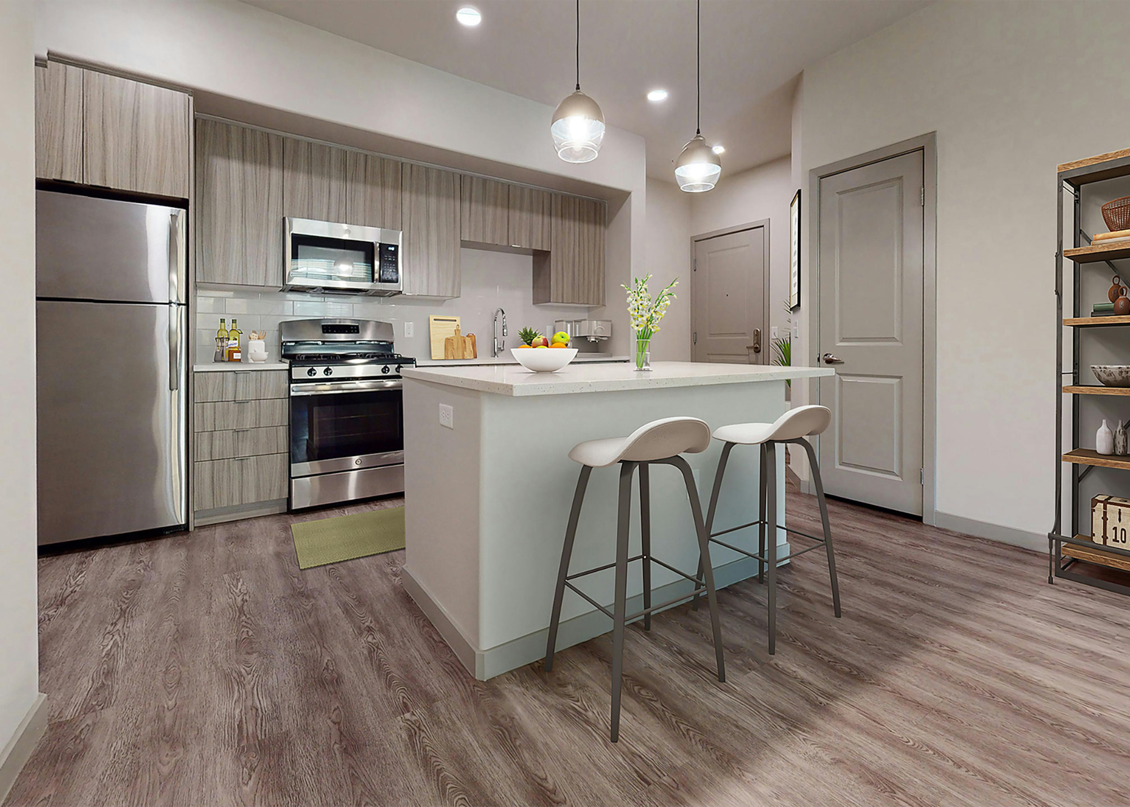Open kitchen at AMLI Camarillo apartments with island seating, pendant lights, stainless steel appliances and modern wood cabinetry.