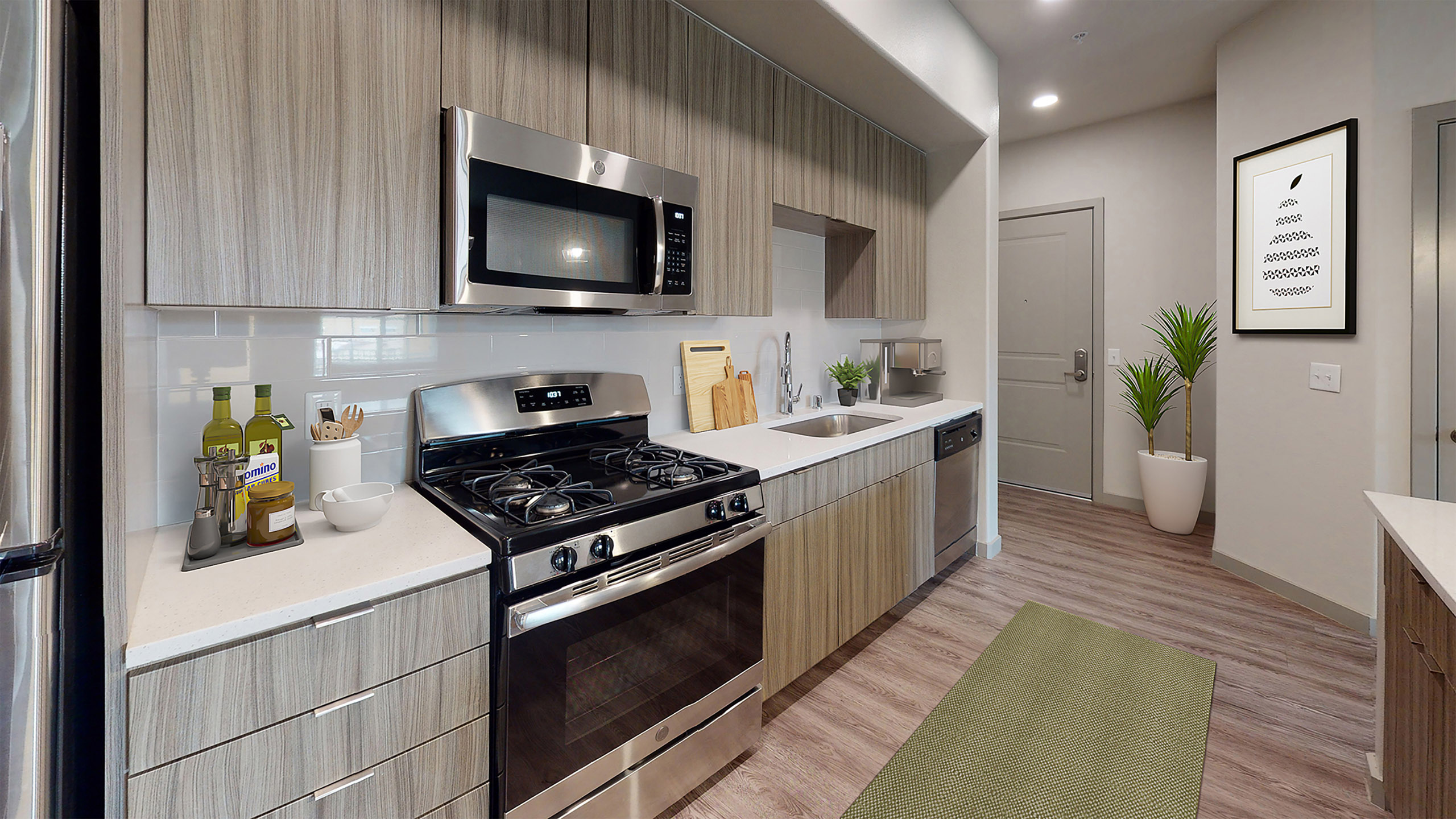 Interior view of AMLI Camarillo apartment kitchen with gas stove, built-in microwave, white tile backsplash, and sleek light wood cabinets.