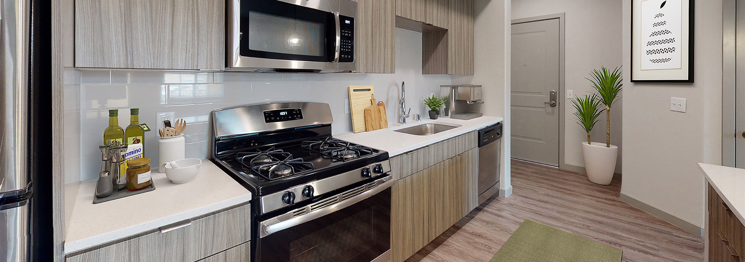 Interior view of AMLI Camarillo apartment kitchen with gas stove, built-in microwave, white tile backsplash, and sleek light wood cabinets.