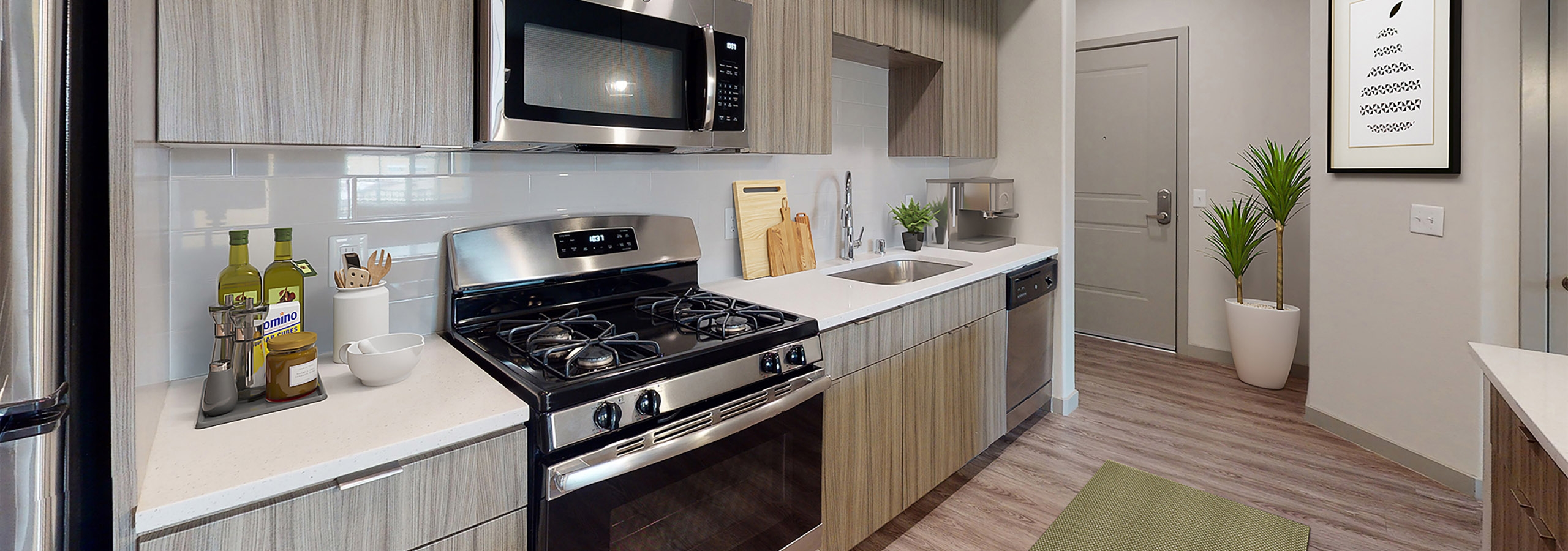 Interior view of AMLI Camarillo apartment kitchen with gas stove, built-in microwave, white tile backsplash, and sleek light wood cabinets.