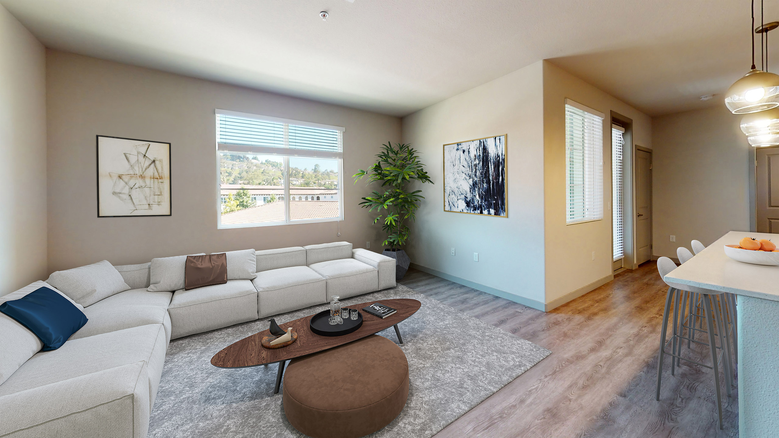 Bright living room at AMLI Camarillo apartments with large light gray sectional sofa, wall art, window with scenic views, and wood floors.