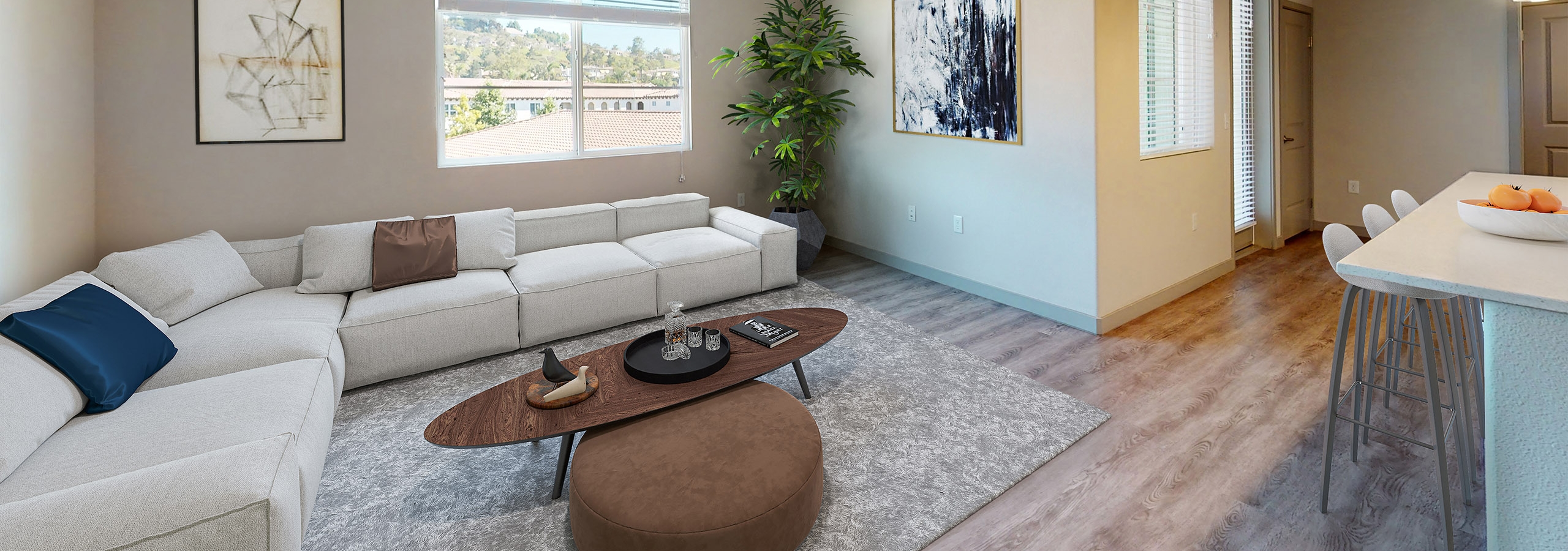 Bright living room at AMLI Camarillo apartments with large light gray sectional sofa, wall art, window with scenic views, and wood floors.