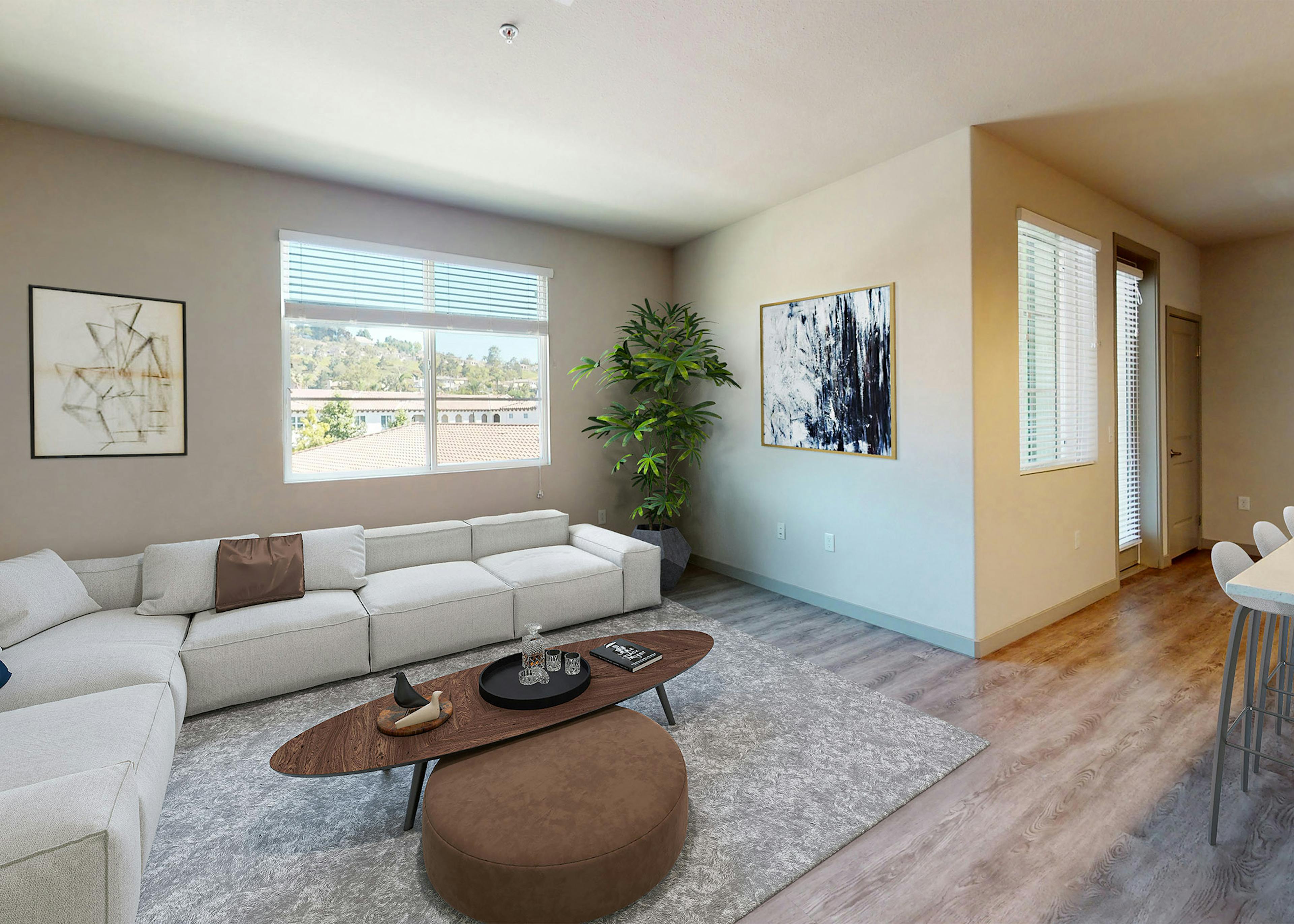 Bright living room at AMLI Camarillo apartments with large light gray sectional sofa, wall art, window with scenic views, and wood floors.