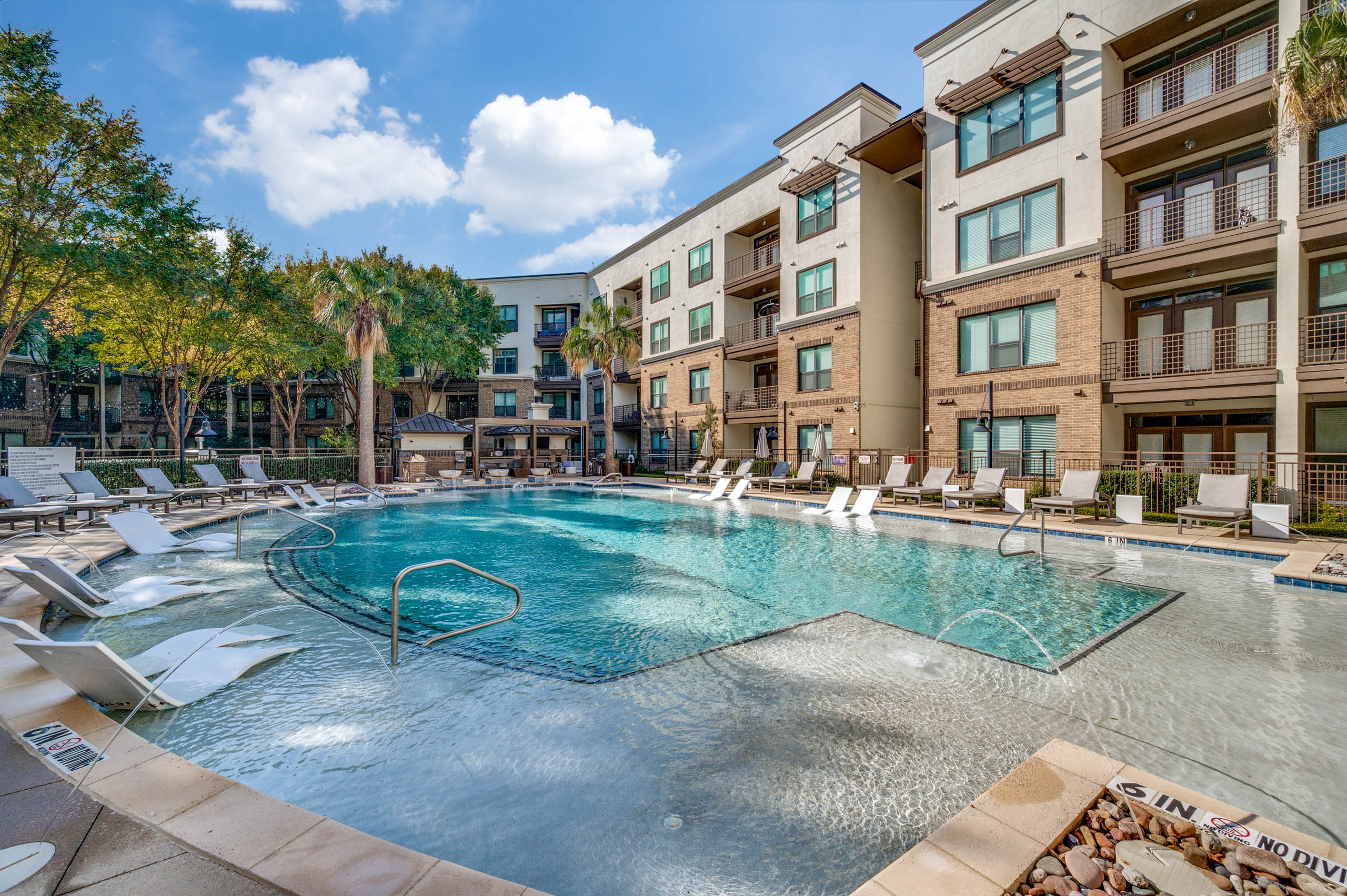 Wide bright view of the resort-style pool with in-water loungers, palm trees, and sun deck at AMLI at the Ballpark apartments.