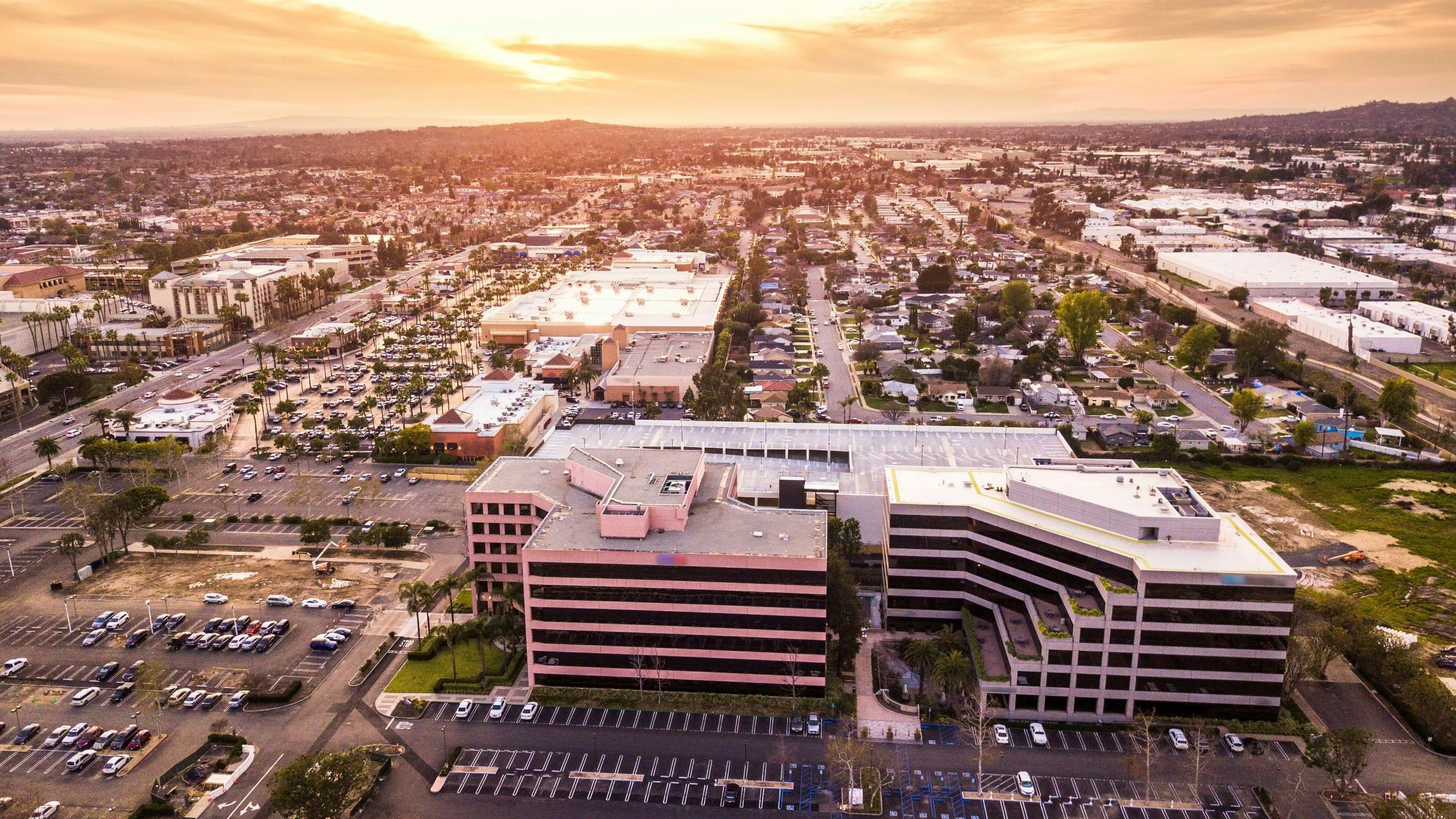 Sunset view of a palm-lined California shopping center under a twilight sky with warm building lights.