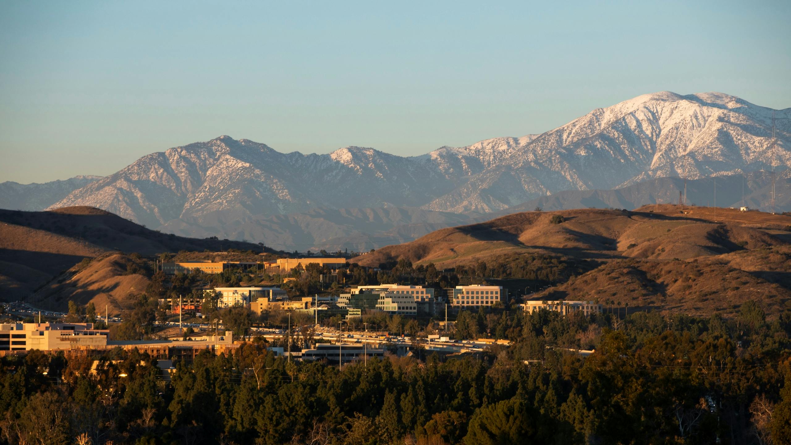 A scenic view of a suburban valley with office buildings and lush trees in the foreground and snow-capped mountains in the distance.