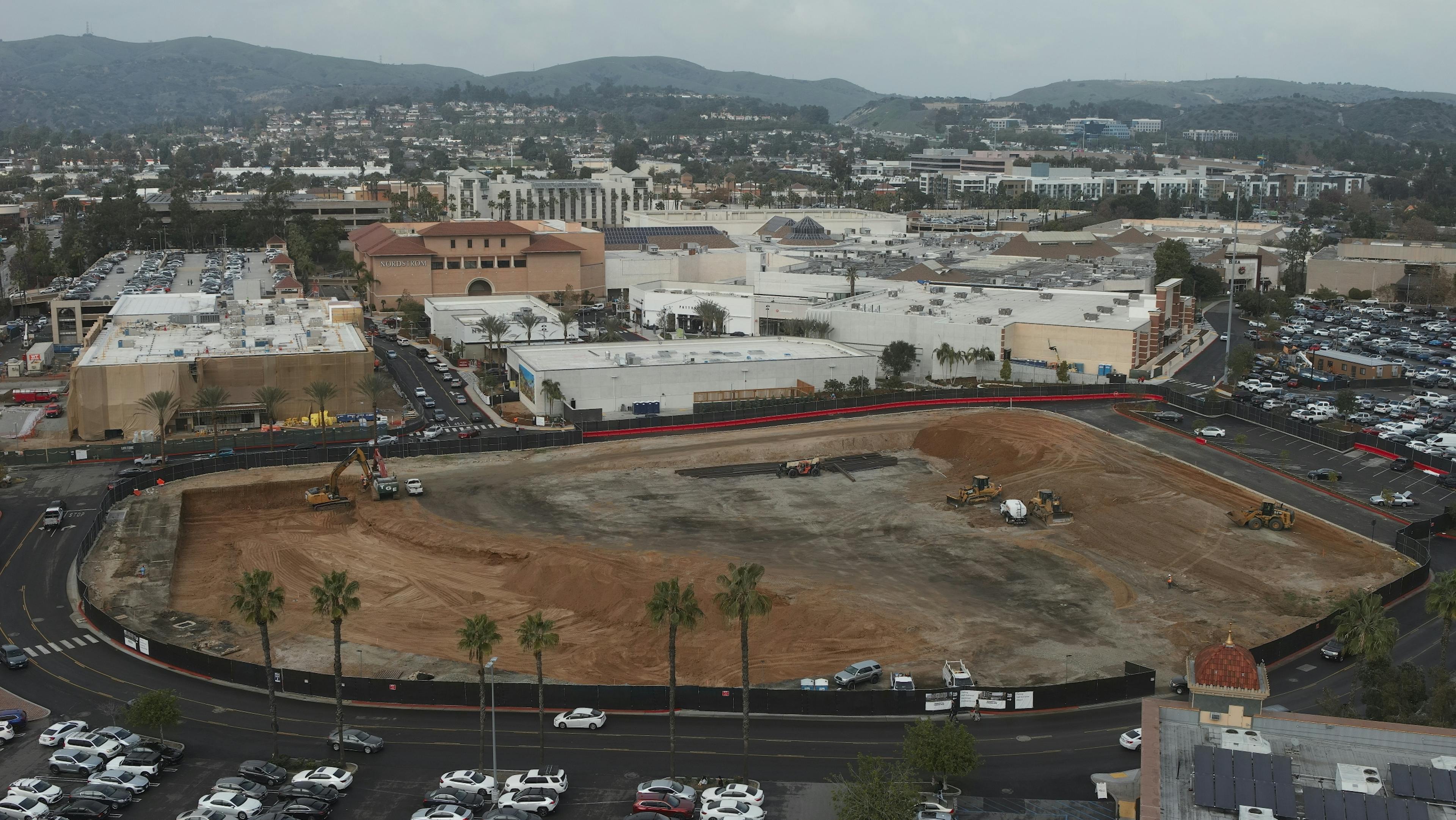 Aerial view of AMLI Brea construction site with excavators and bulldozers positioned around the dirt with surrounding black fence