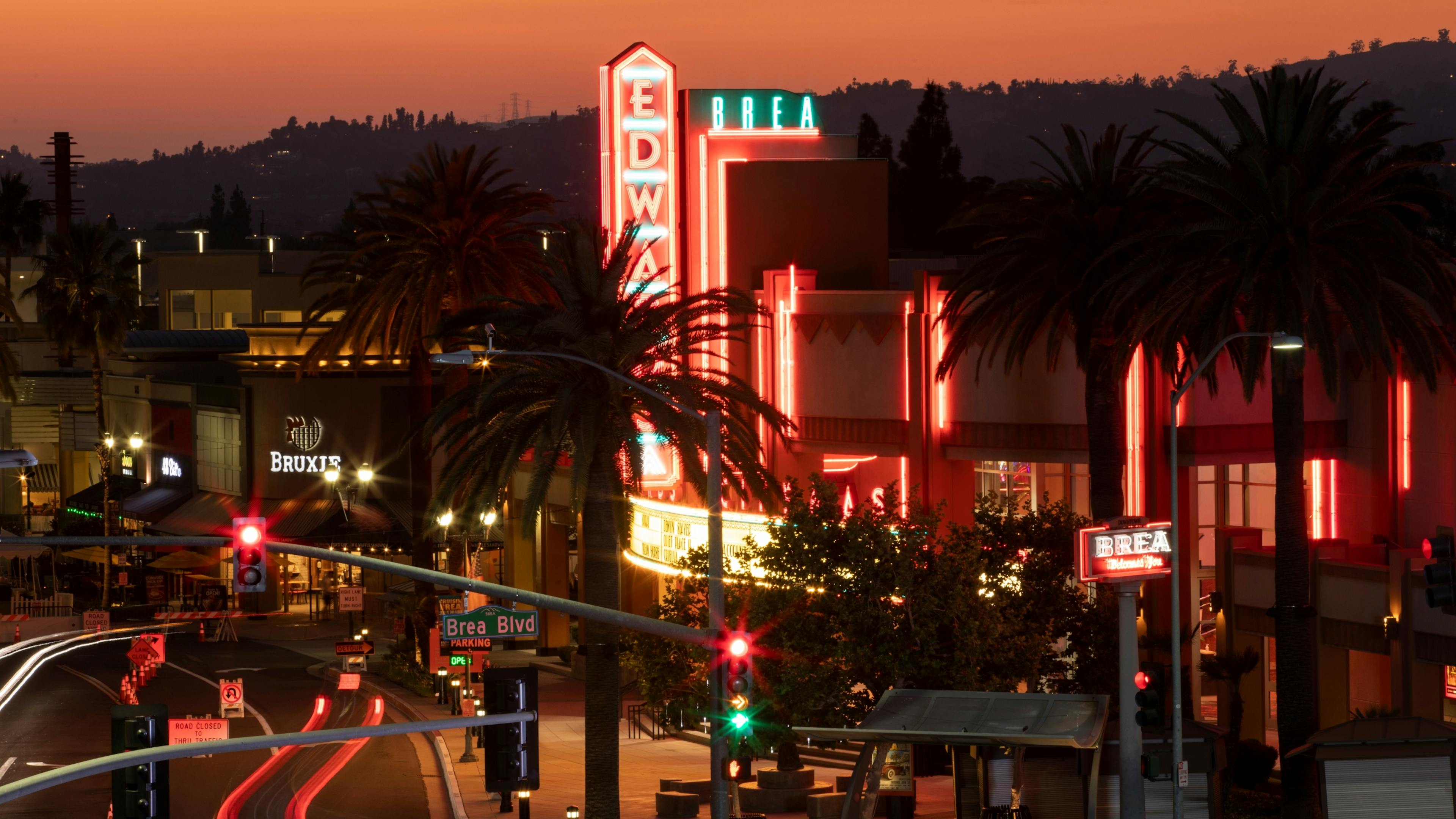 Vibrant nighttime view of the Edwards Brea West movie theater with glowing neon signs and light trails on Brea Blvd at sunset.