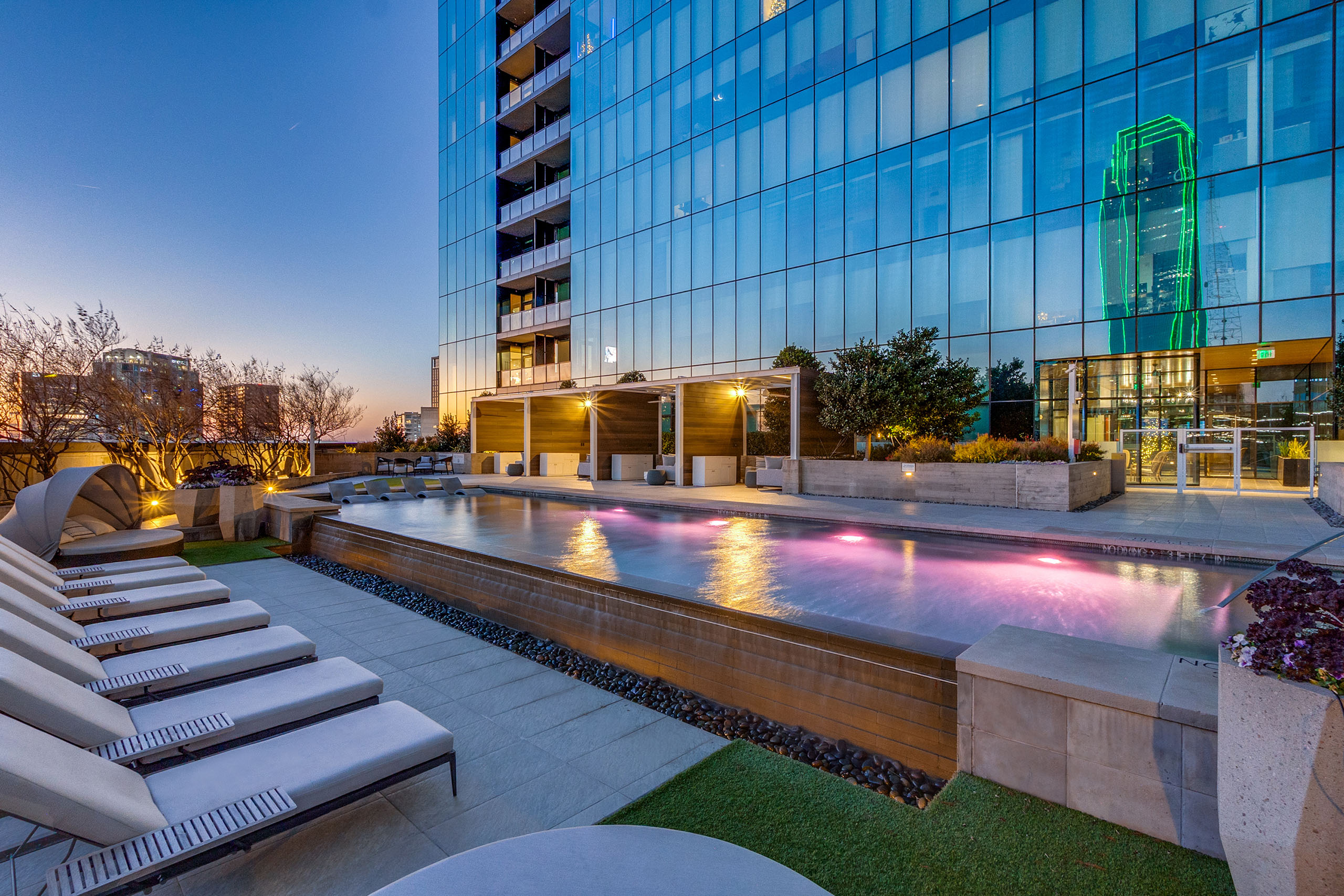 Waterfall edge pool cascading at AMLI Fountain Place with glass tower and blue windows with apartments in background and loungers.