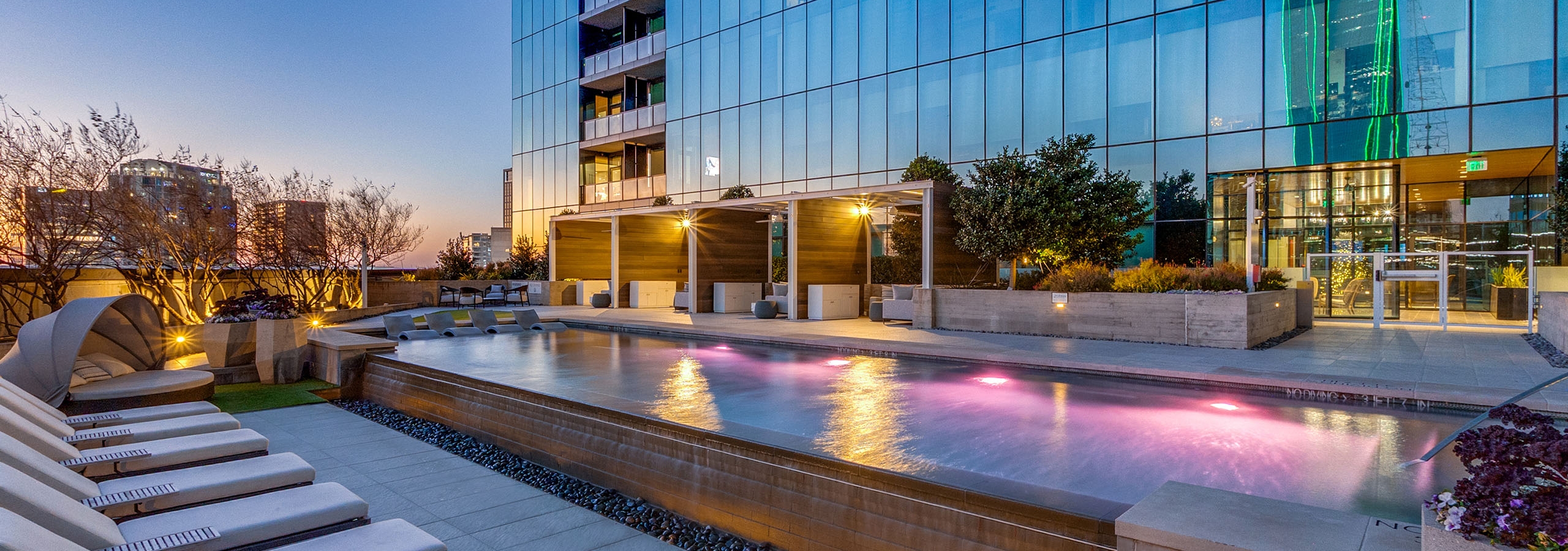 Waterfall edge pool cascading at AMLI Fountain Place with glass tower and blue windows with apartments in background and loungers.