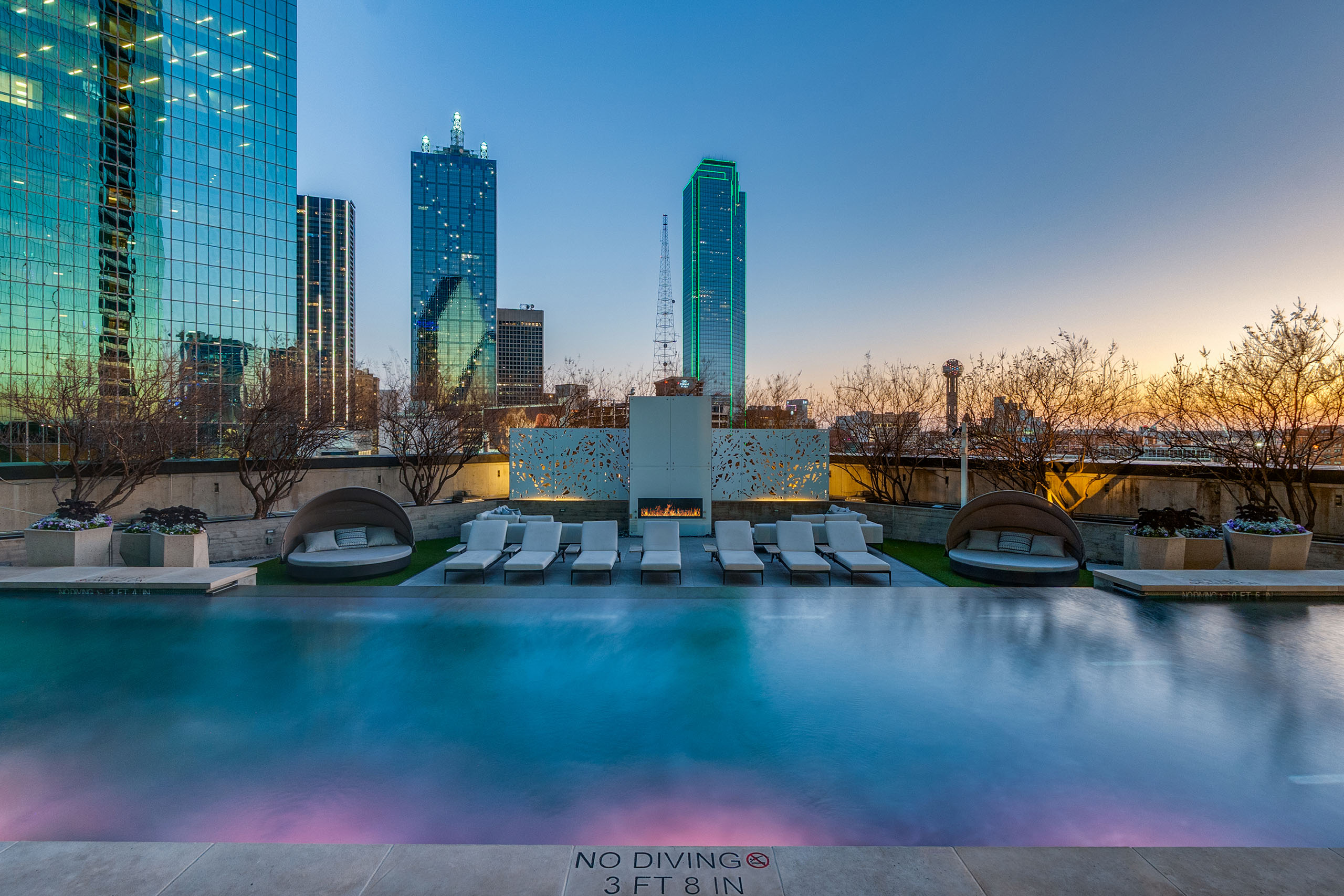 AMLI Fountain Place pool with mood lighting, fireplace and loungers at sunset overlooking downtown Dallas skyline high rises.