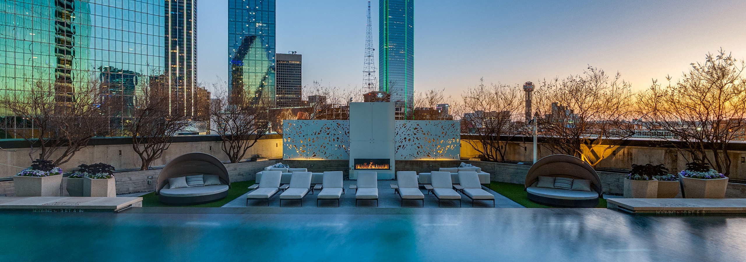 AMLI Fountain Place pool with mood lighting, fireplace and loungers at sunset overlooking downtown Dallas skyline high rises.
