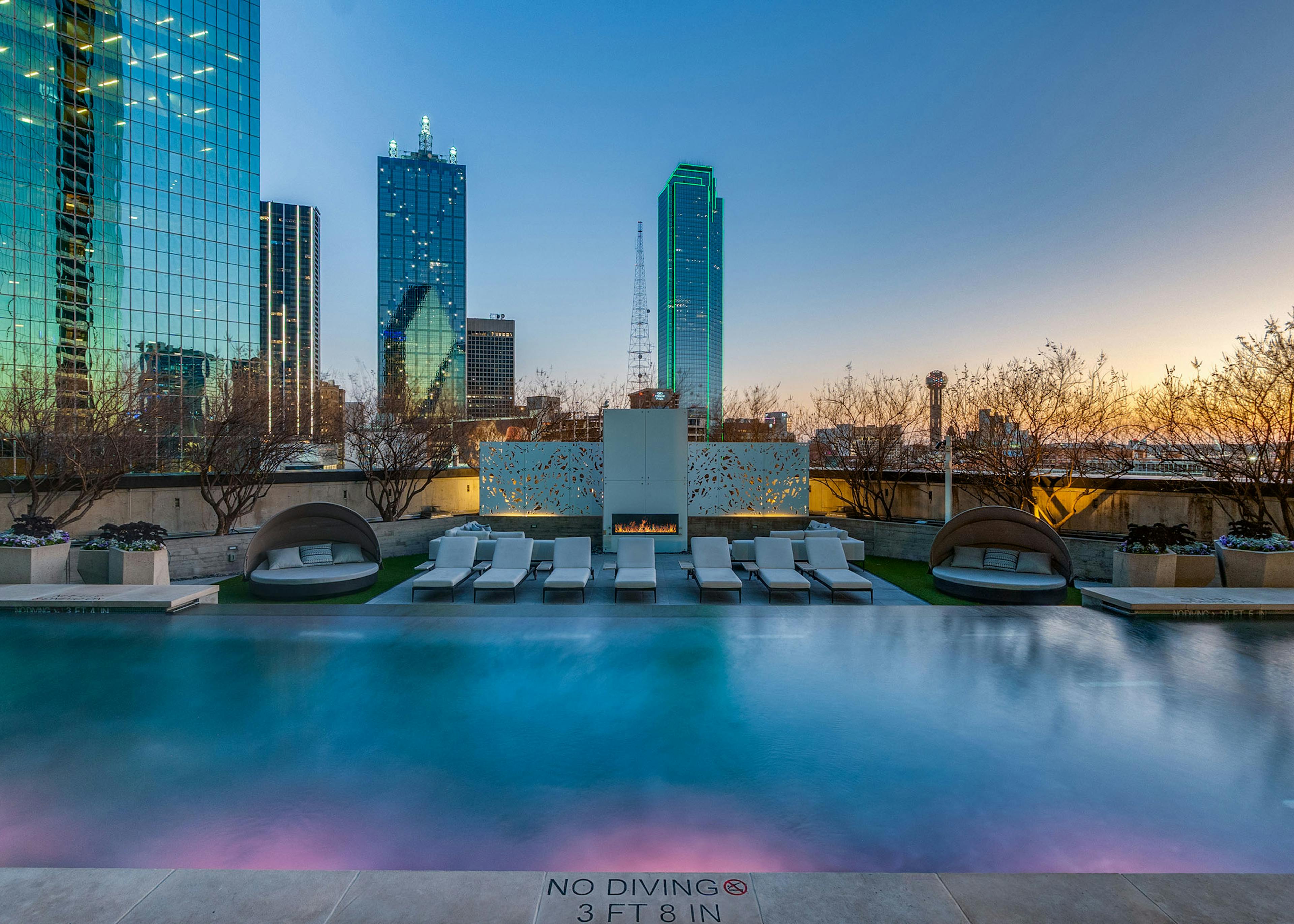 AMLI Fountain Place pool with mood lighting, fireplace and loungers at sunset overlooking downtown Dallas skyline high rises.