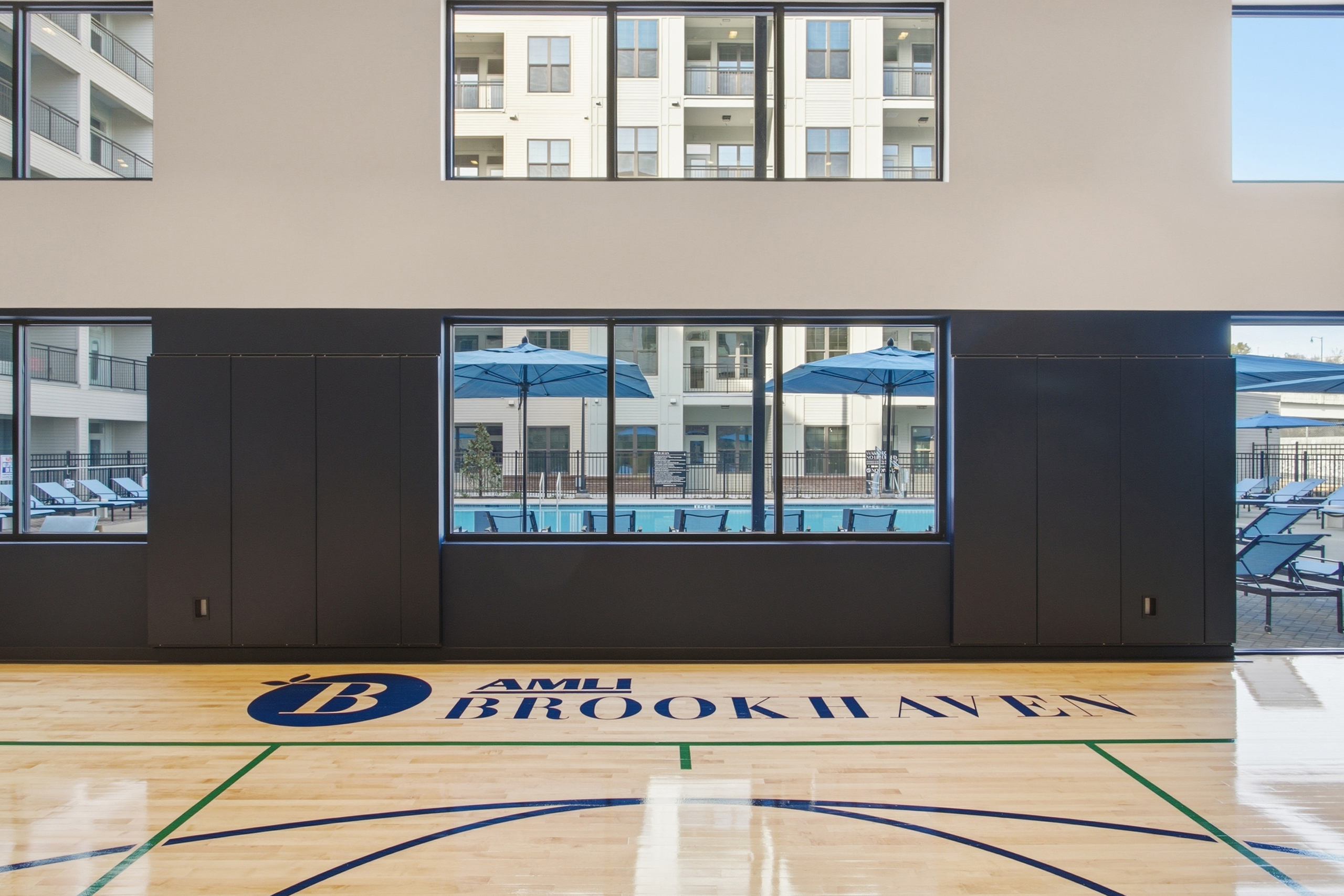 Indoor sport court at AMLI Brookhaven overlooking a swimming pool deck with lounge chairs.