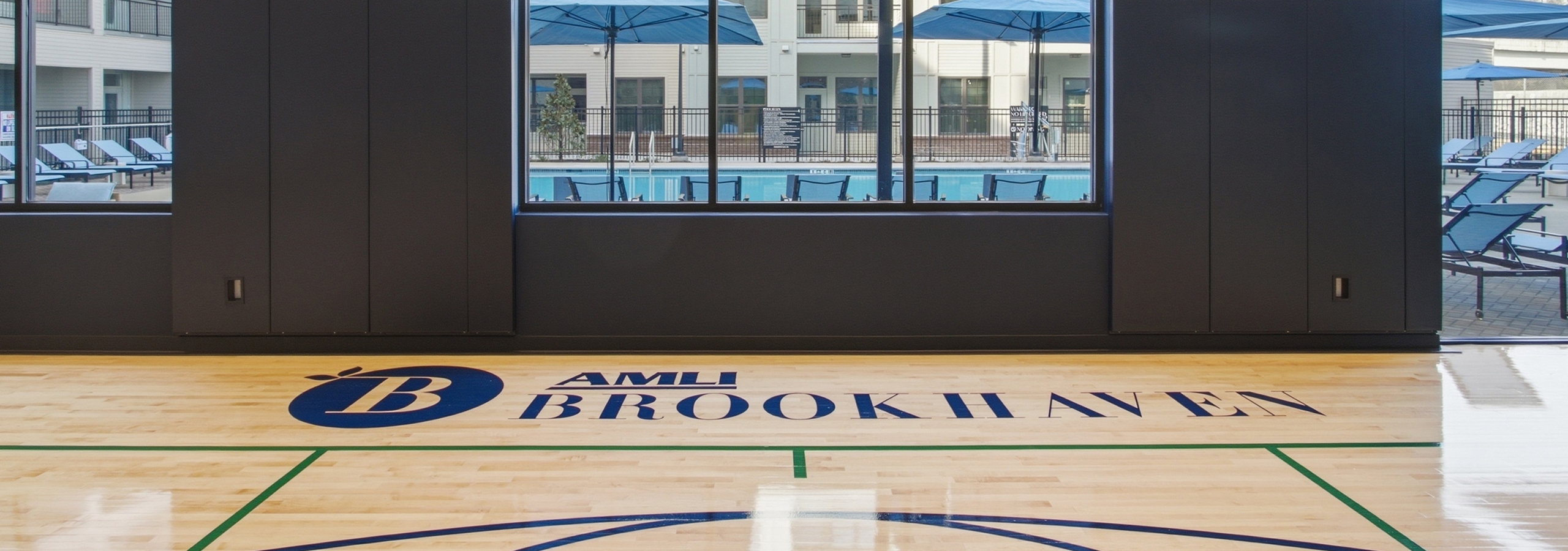 Indoor sport court at AMLI Brookhaven overlooking a swimming pool deck with lounge chairs.