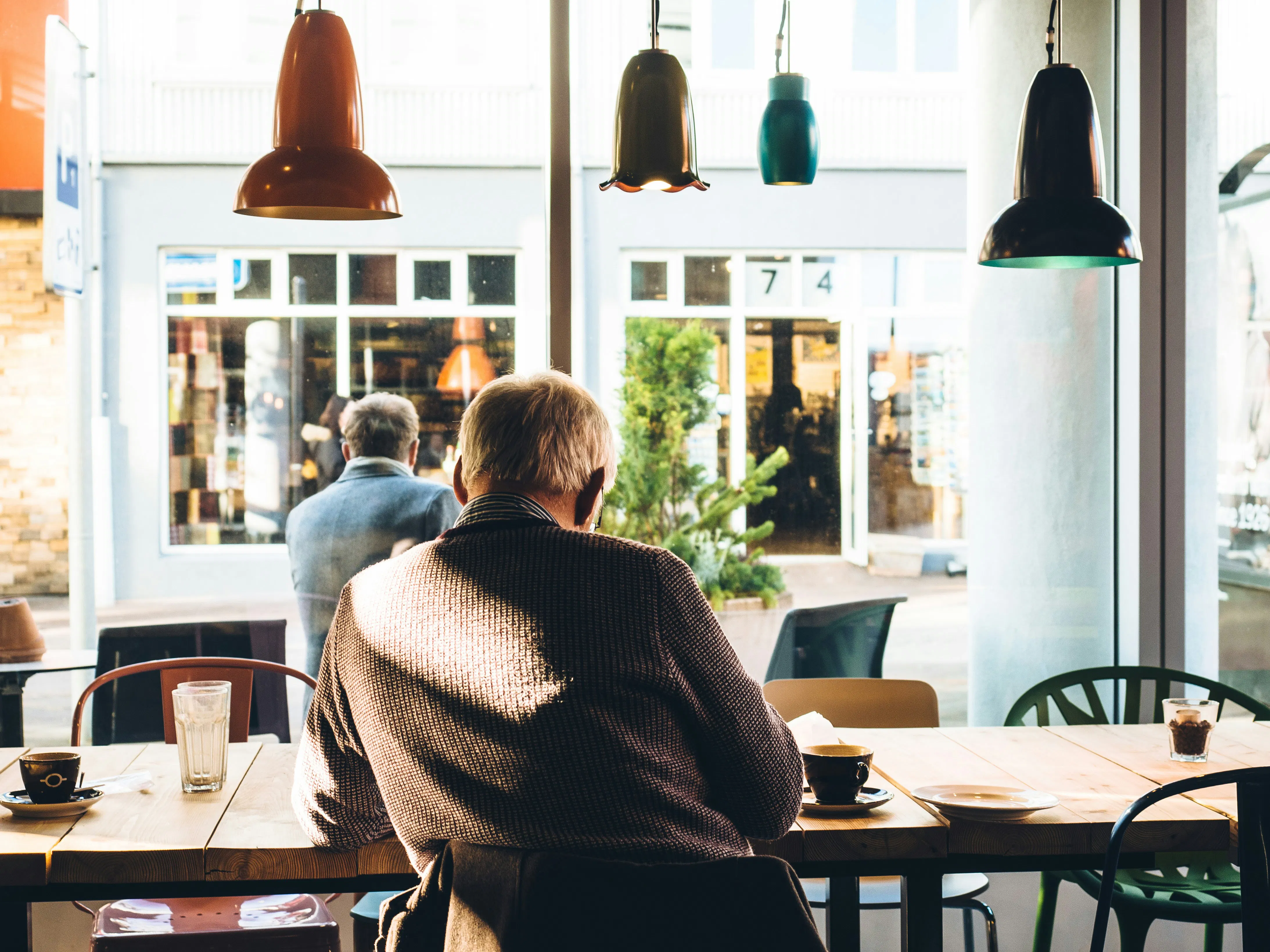 A peaceful high-angle shot of an older man seated at a wooden cafe table, enjoying a quiet moment with coffee by a bright window.