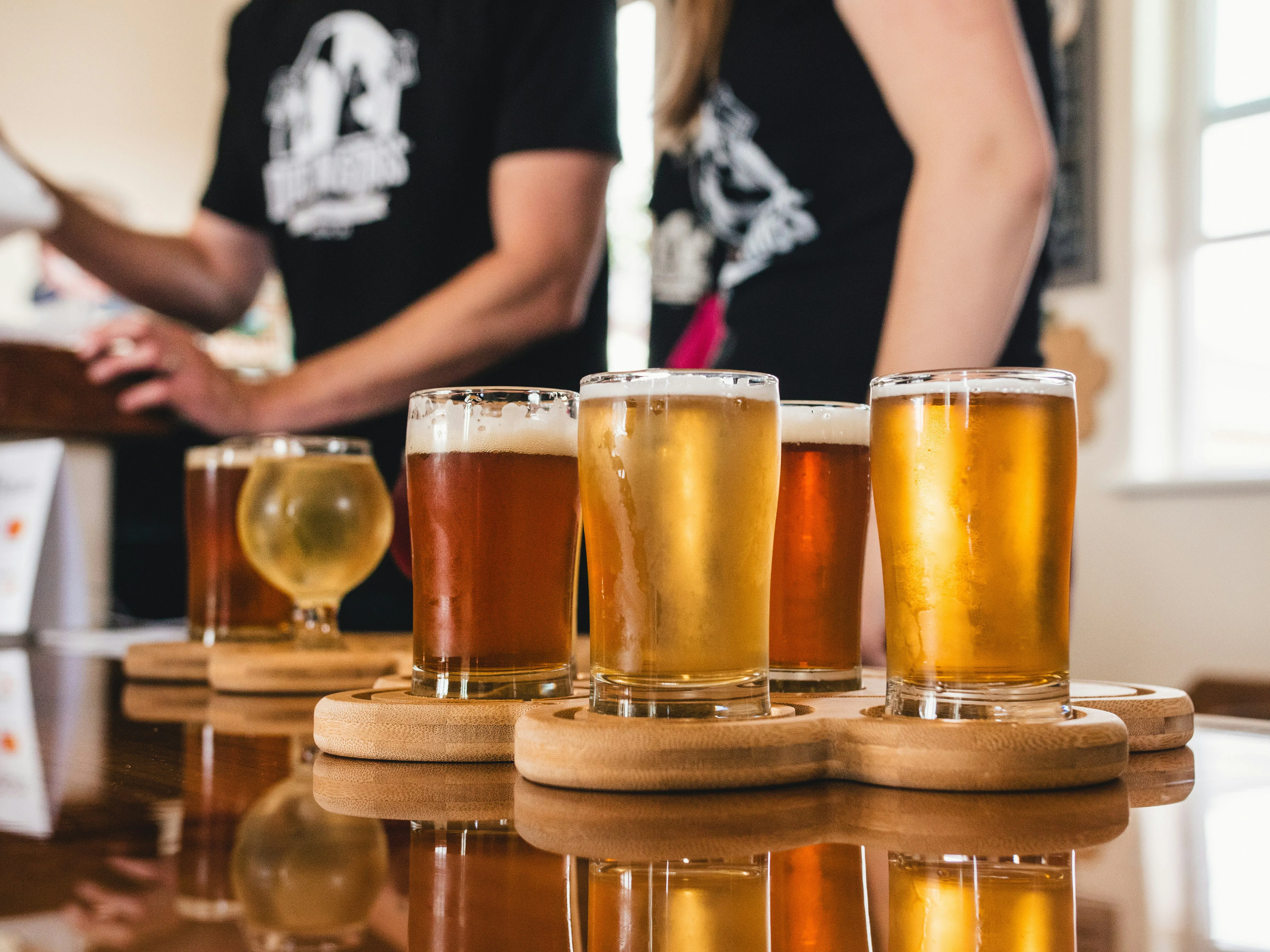 A close-up of a craft beer flight on a wooden paddle, showcasing a variety of brews from light ales to dark stouts at a local brewery.